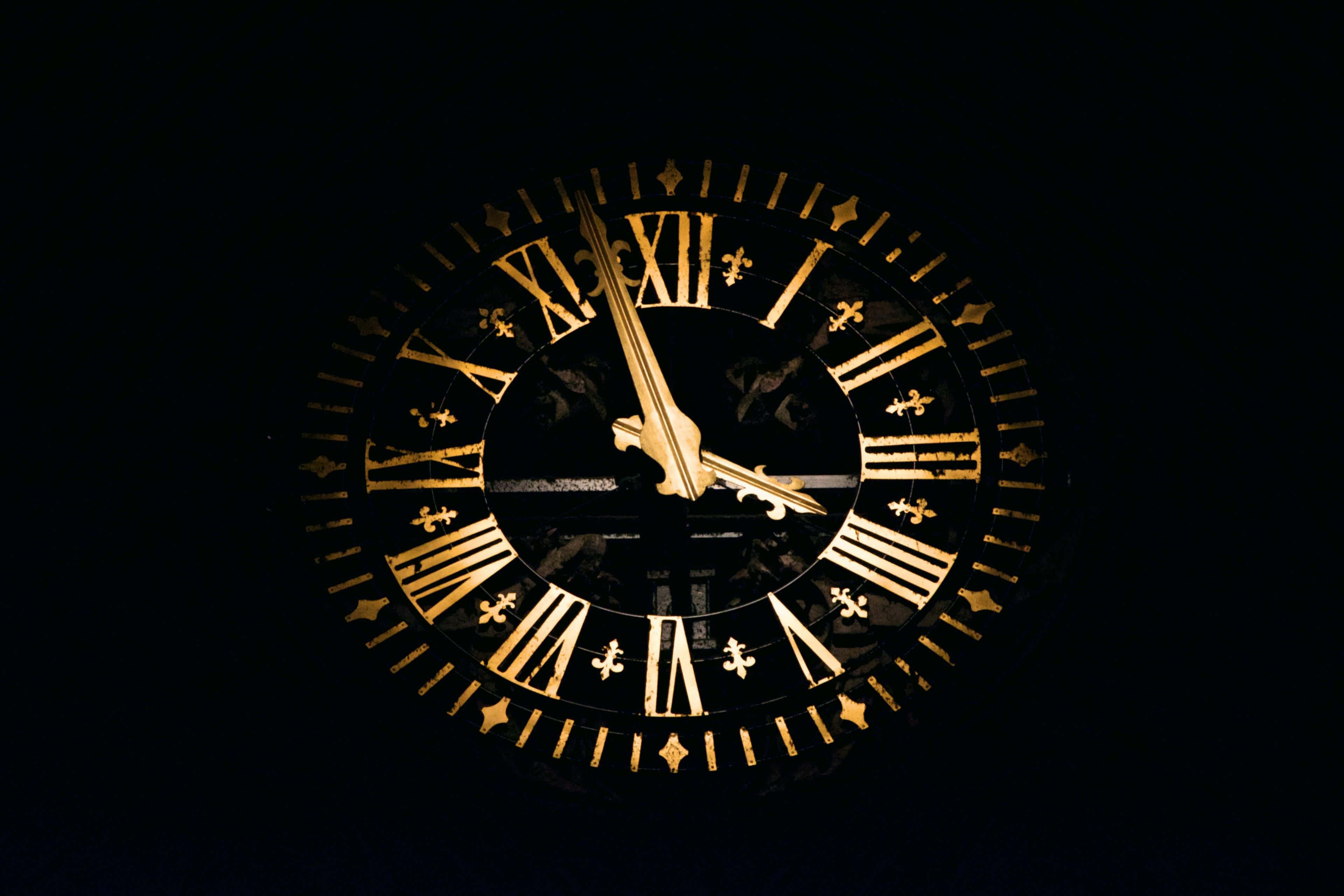 Time 桌布 壁紙 — 一個金色華麗的時鐘，帶有羅馬數字和百合花飾，在漆黑的背景中閃耀。
