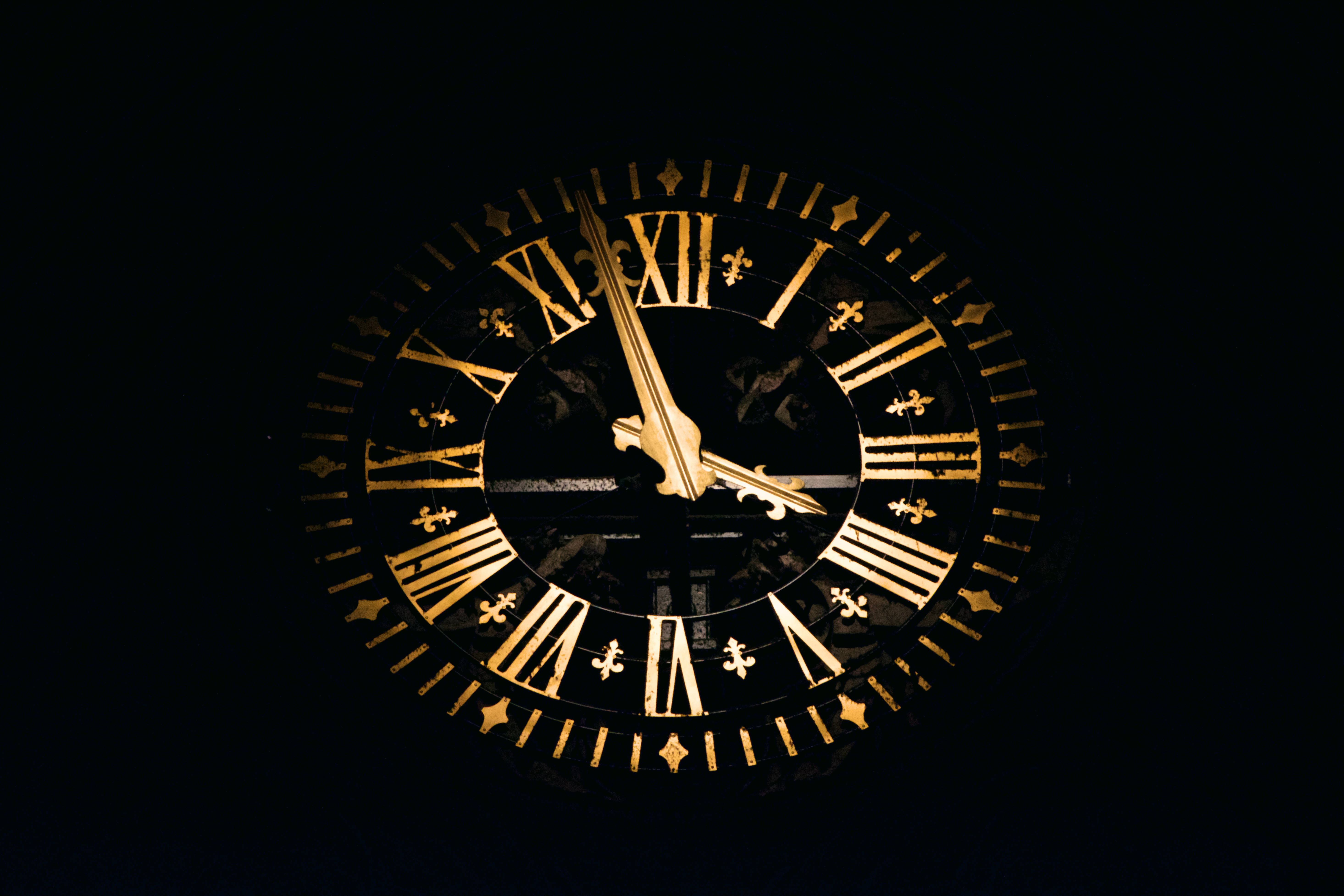 Clock 桌布 壁紙 — 一個金色華麗的時鐘，帶有羅馬數字和鳶尾花標記，在漆黑的背景下發光。