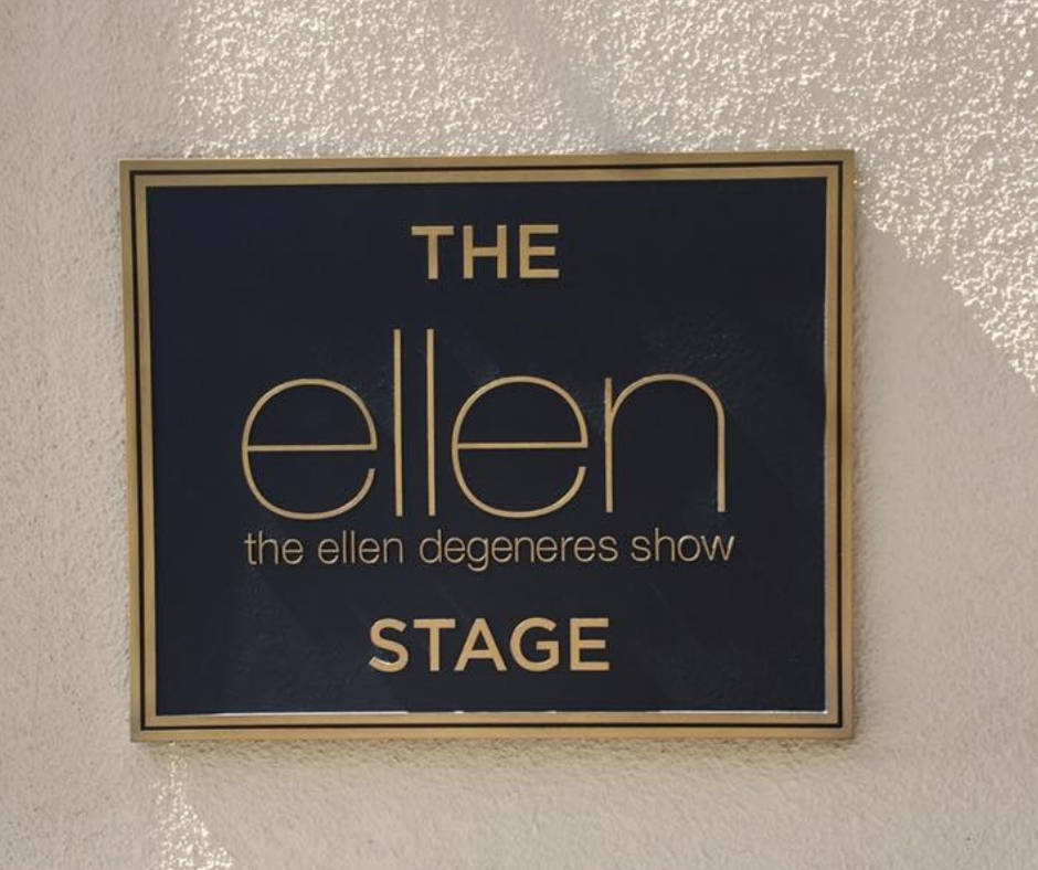Celebrity 桌布 壁紙 — 一個金色邊框的標誌，上面寫著「THE ellen the ellen degeneres show STAGE」，安裝在有紋理的牆上，陽光投射出陰影。