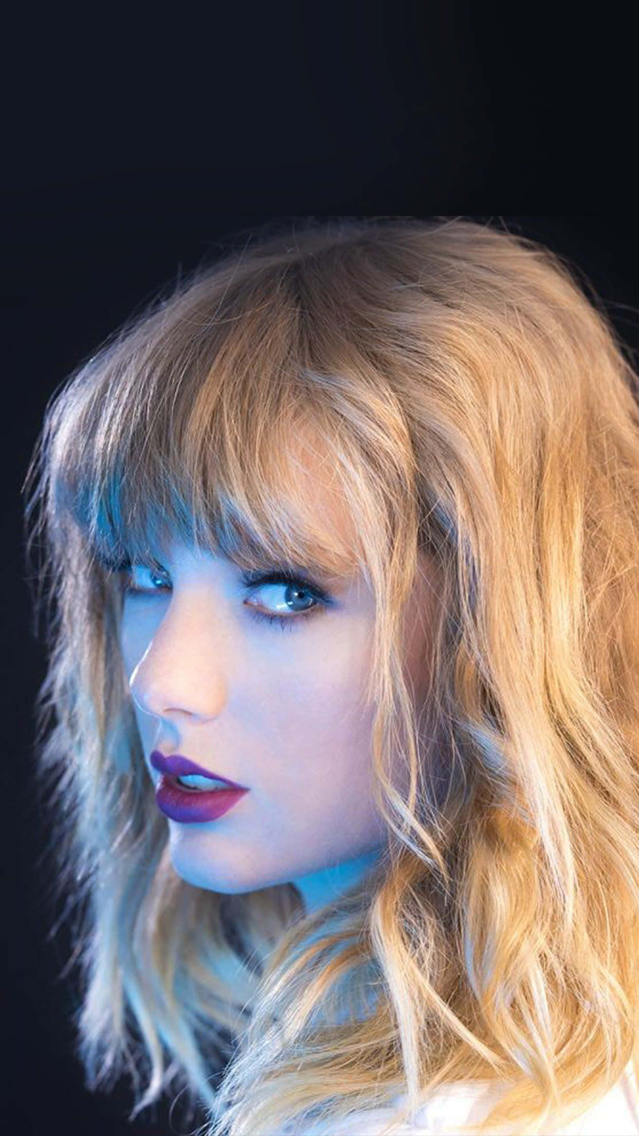 Taylor Swift iPhone 桌布 壁紙 — 一個金髮、紅唇的女性在深色背景前的特寫肖像。