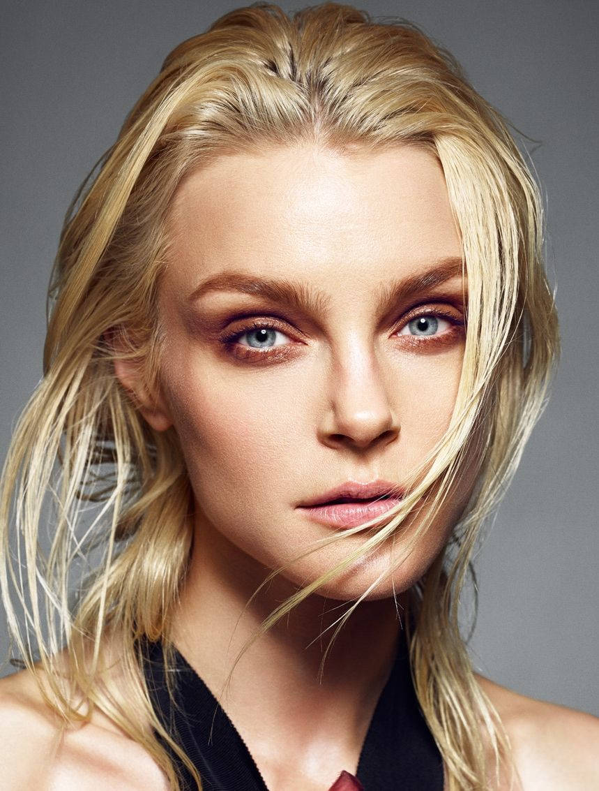 jessica stam 桌布 壁紙 — 一個金髮女人的特寫肖像，擁有引人注目的藍色眼睛和風吹亂的頭髮，背景是中性灰色。