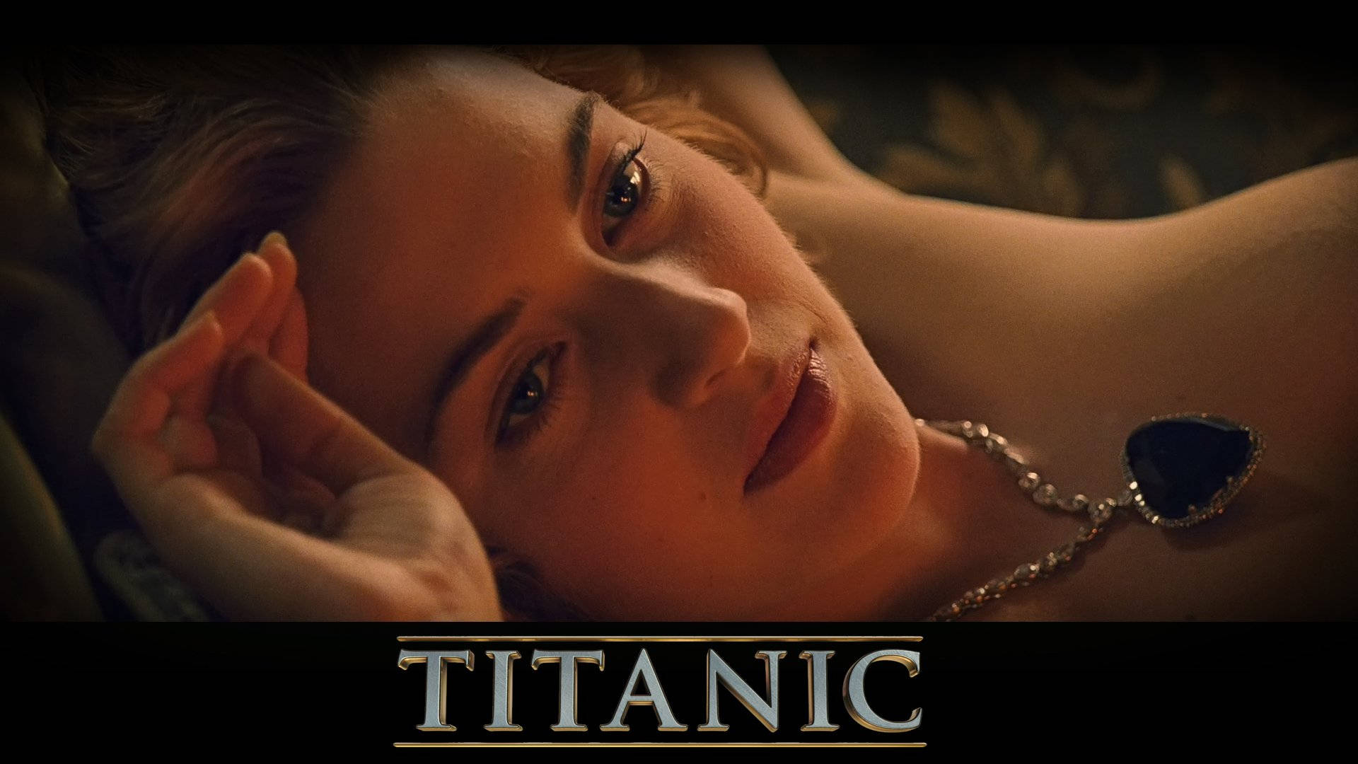 Kate Winslet 桌布 壁紙 — 一個金髮女子戴著心形吊墜，在溫暖的電影燈光下將頭靠在手上的特寫。