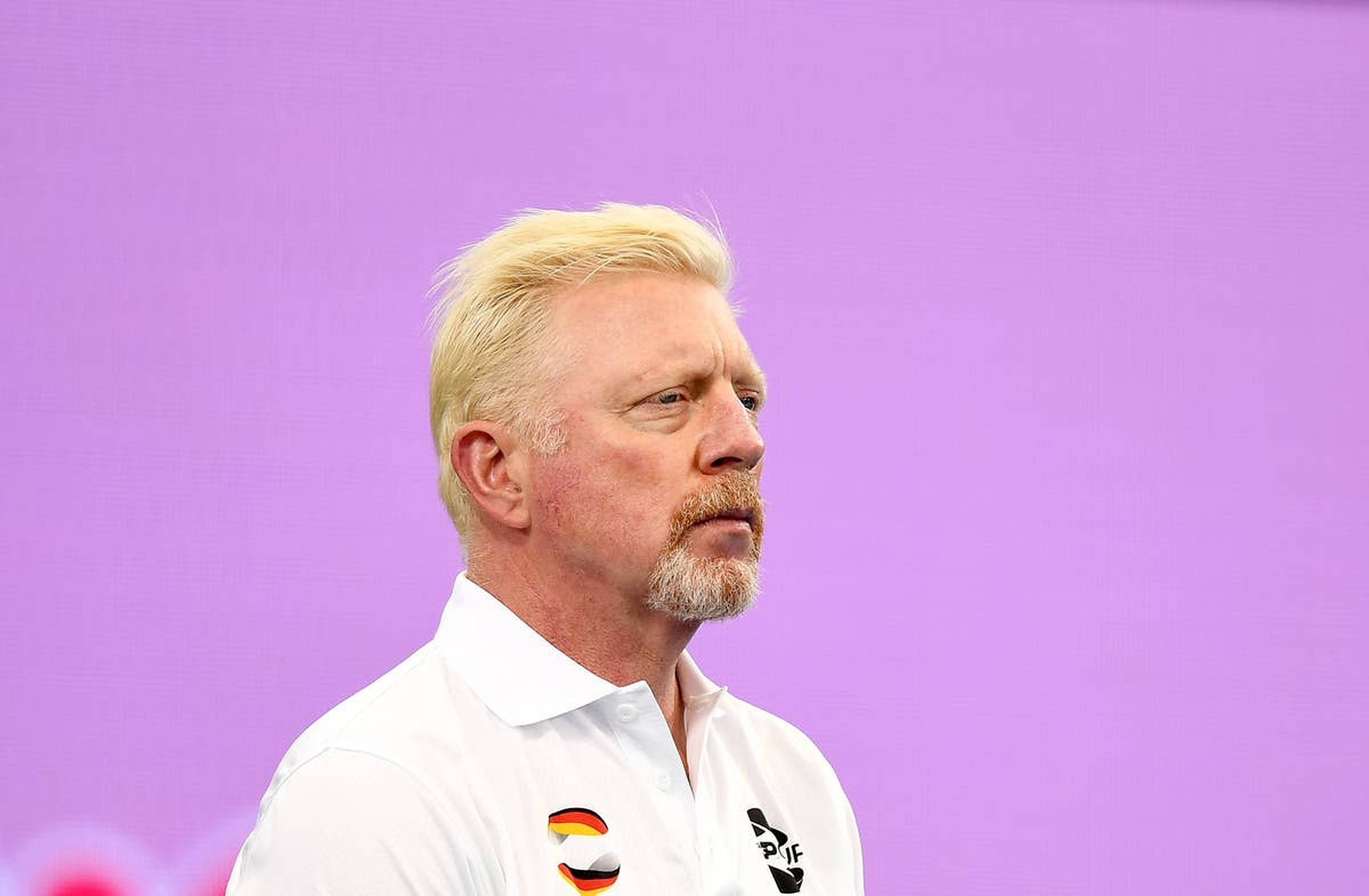 Boris Becker 桌布 壁紙 — 一個金髮留山羊鬍的男人穿著白色Polo衫，站在純紫色背景前。