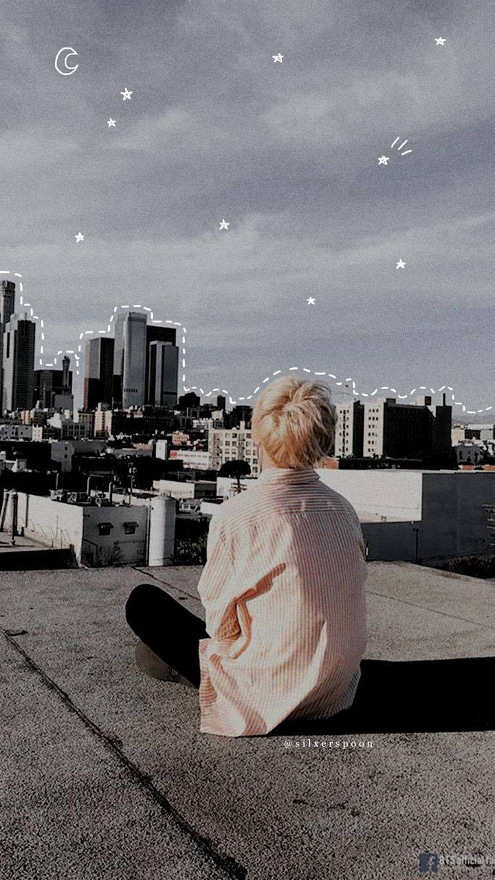 BTS 桌布 壁紙 — 一個金髮的人坐在屋頂上，俯瞰著星空下新月映襯的城市天際線。