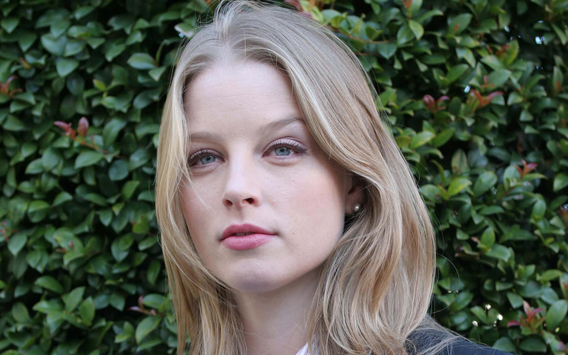 rachel nichols 桌布 壁紙 — 一個金髮碧眼的女人在茂密的綠色樹籬背景下平靜地凝視的特寫肖像。