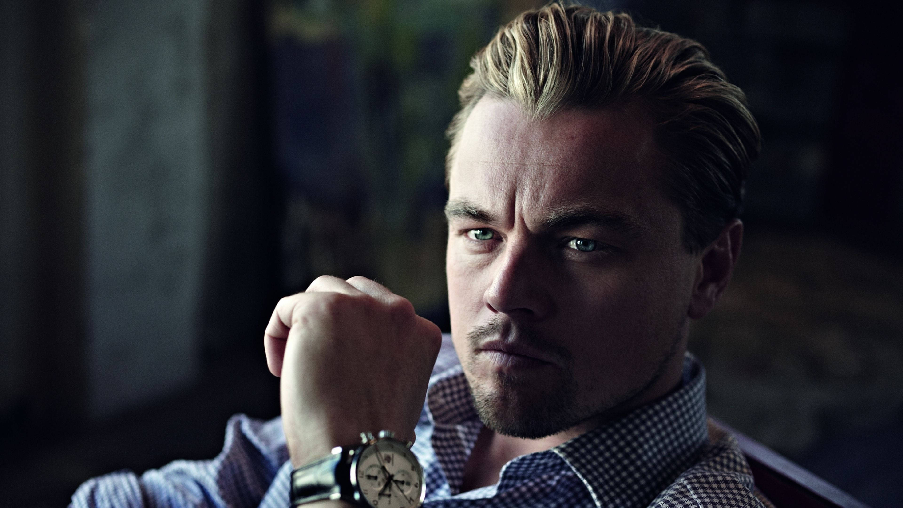 Dicaprio 桌布 壁紙 — 一個金髮綠眼的男人，穿著格紋襯衫和手錶，拳頭托著下巴，專注地凝視。