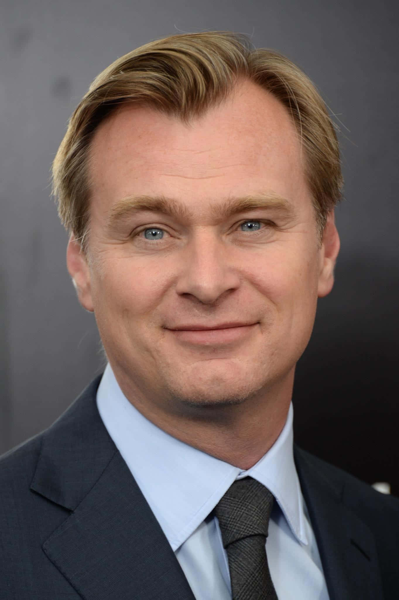 Christopher Nolan 桌布 壁紙 — 一個金髮藍眼男人的特寫肖像，穿著深色西裝和領帶，背景為灰色。