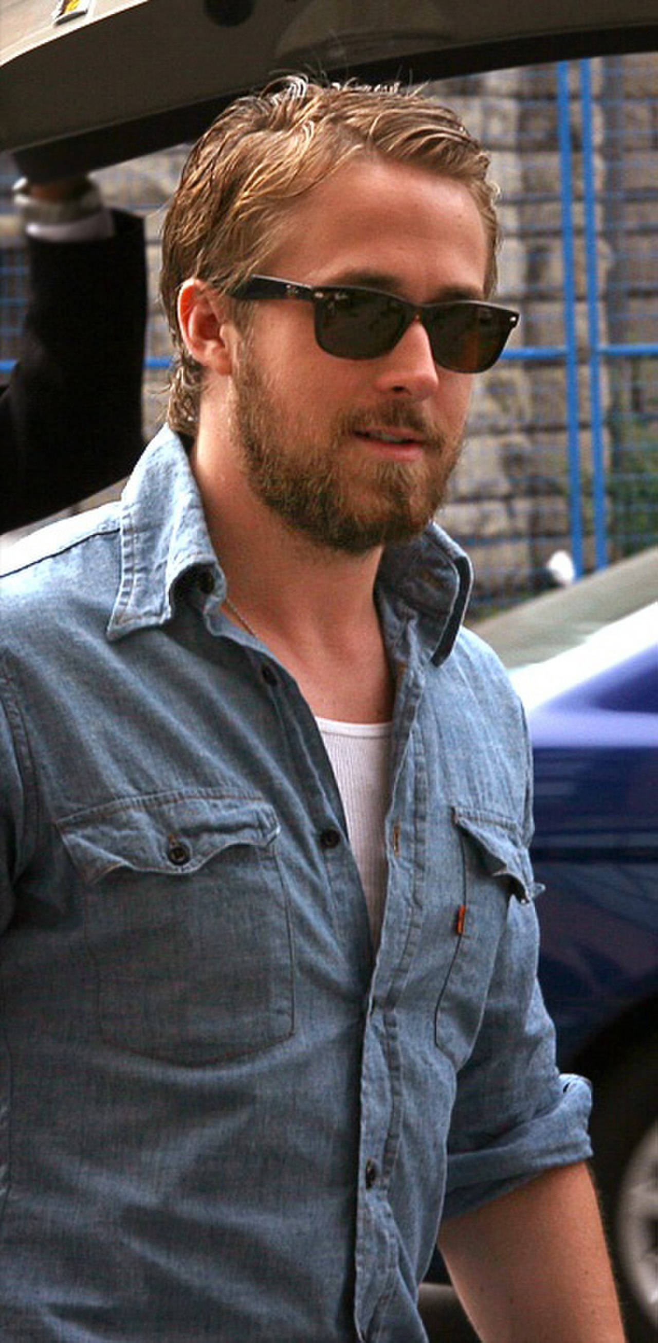 Ryan Gosling 桌布 壁紙 — 一個金髮鬍鬚男戴著太陽眼鏡和牛仔衫，站在一輛車附近。