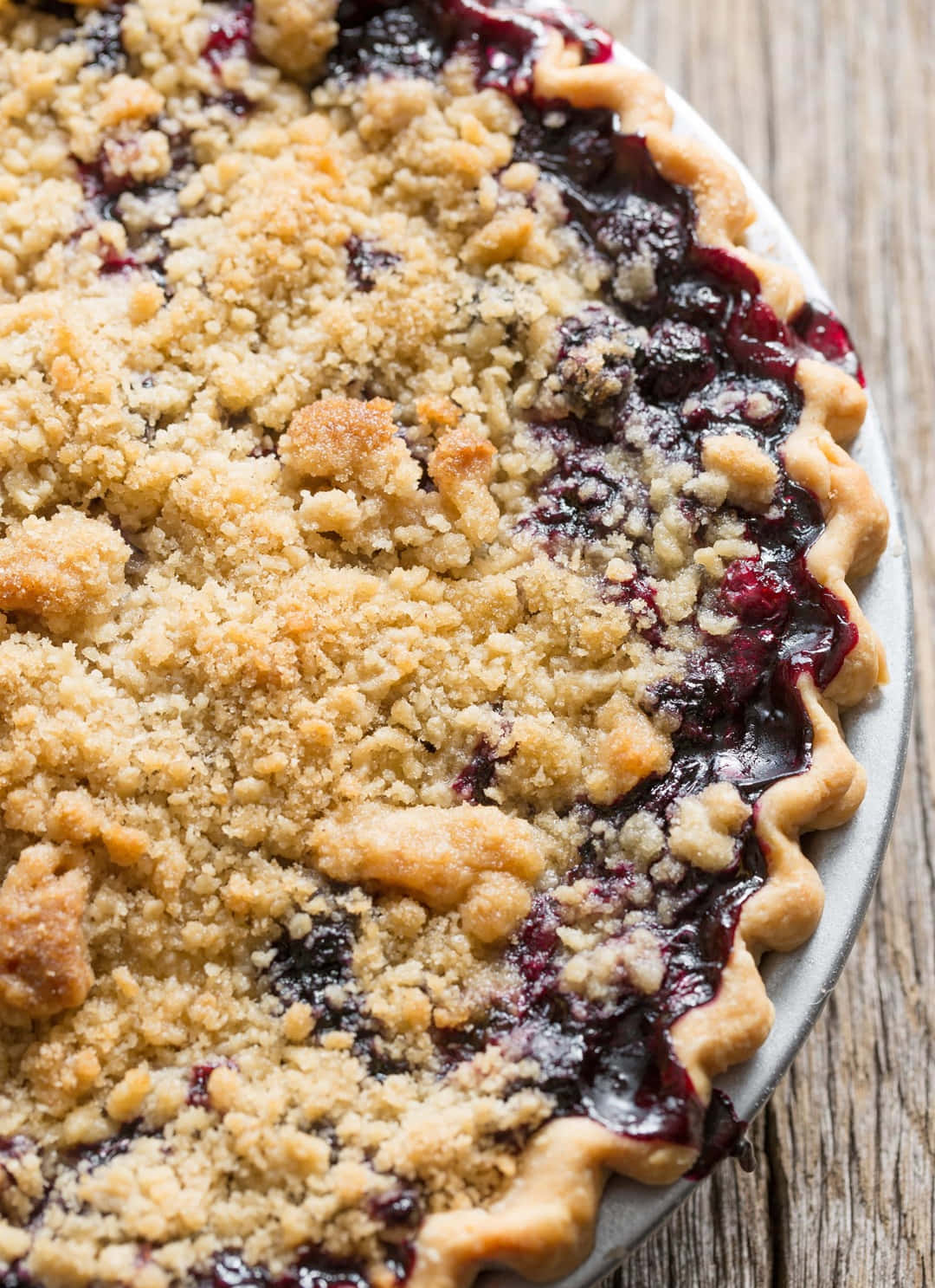 Blueberry Pie 桌布 壁紙 — 一個金黃色、鬆脆的藍莓派特寫，內有冒泡的深色水果餡料，放在質樸的木桌上。