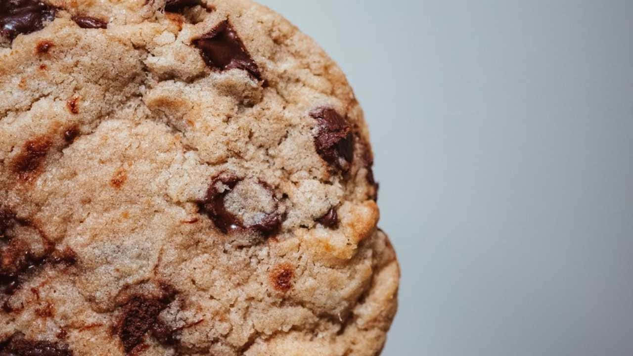 720p Cookies 桌布 壁紙 — 一個金黃色巧克力餅乾的特寫，帶有融化巧克力塊，背景為柔和灰色。