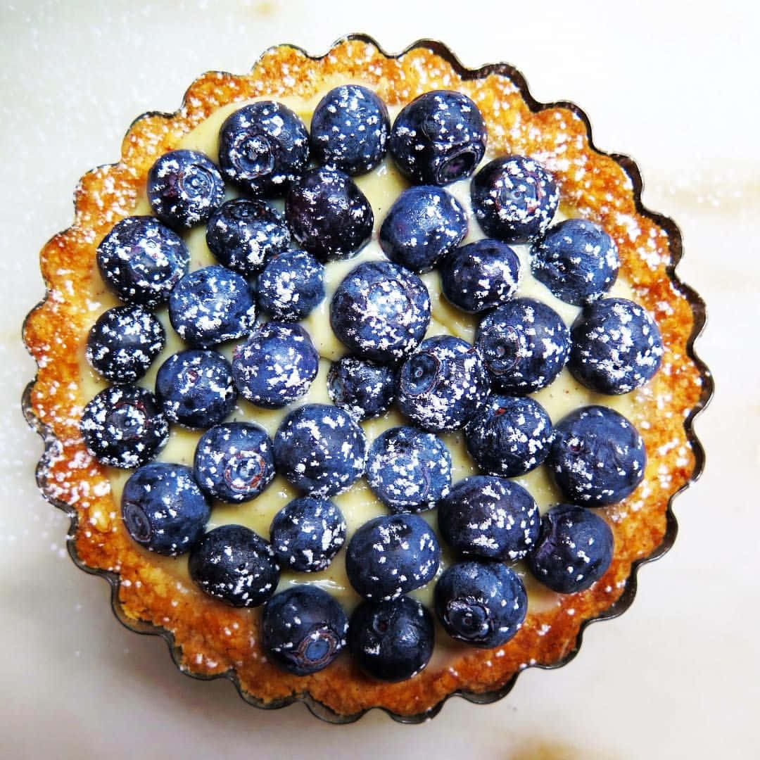 Blueberries Tart 桌布 壁紙 — 一個金黃色撻的特寫，上面鋪滿飽滿的藍莓，撒上糖粉。