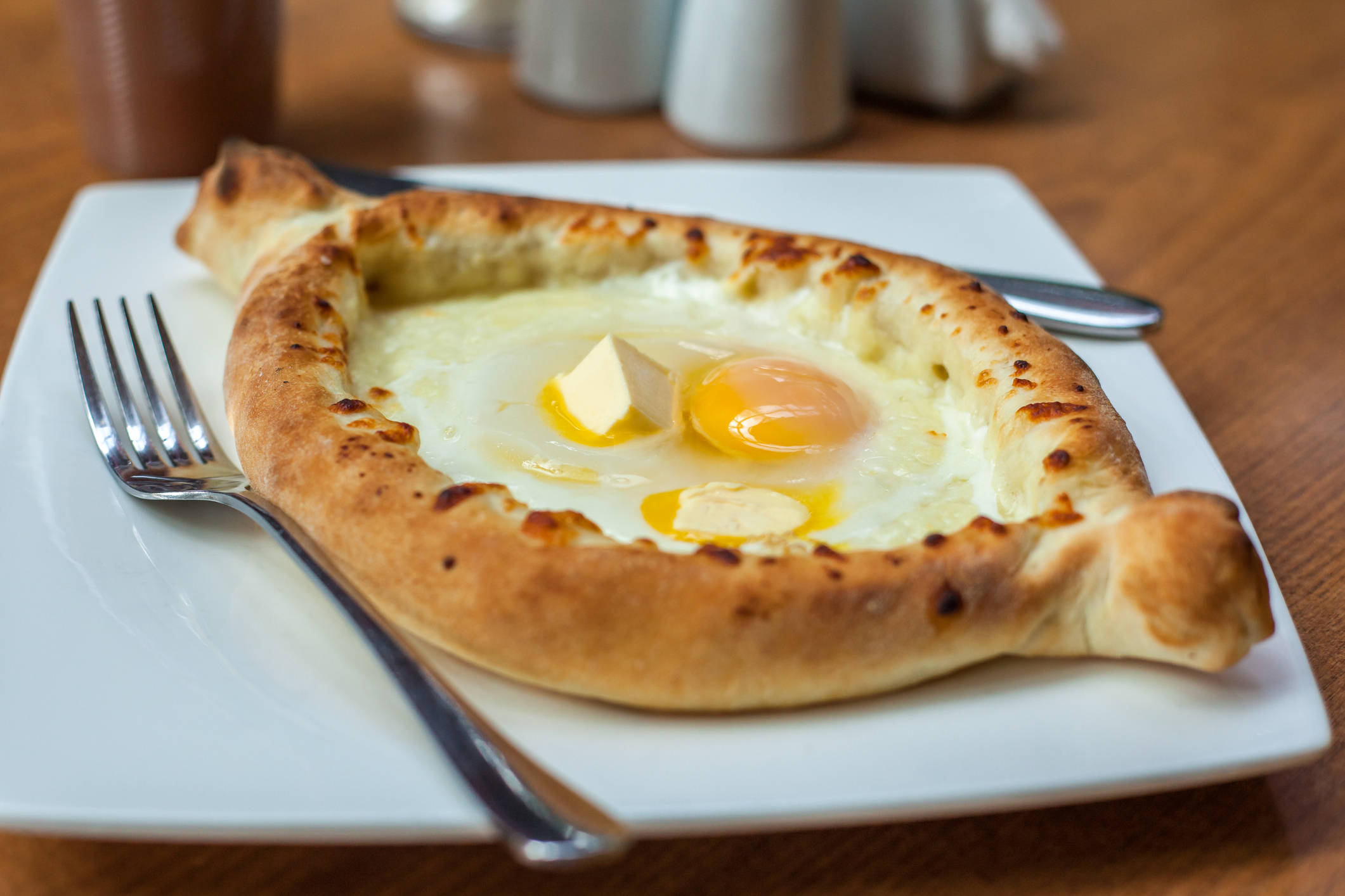 Cheese 桌布 壁紙 — 一個金黃色的 khachapuri 麵包碗，盛載著太陽蛋和融化奶油，放在白色盤子上。