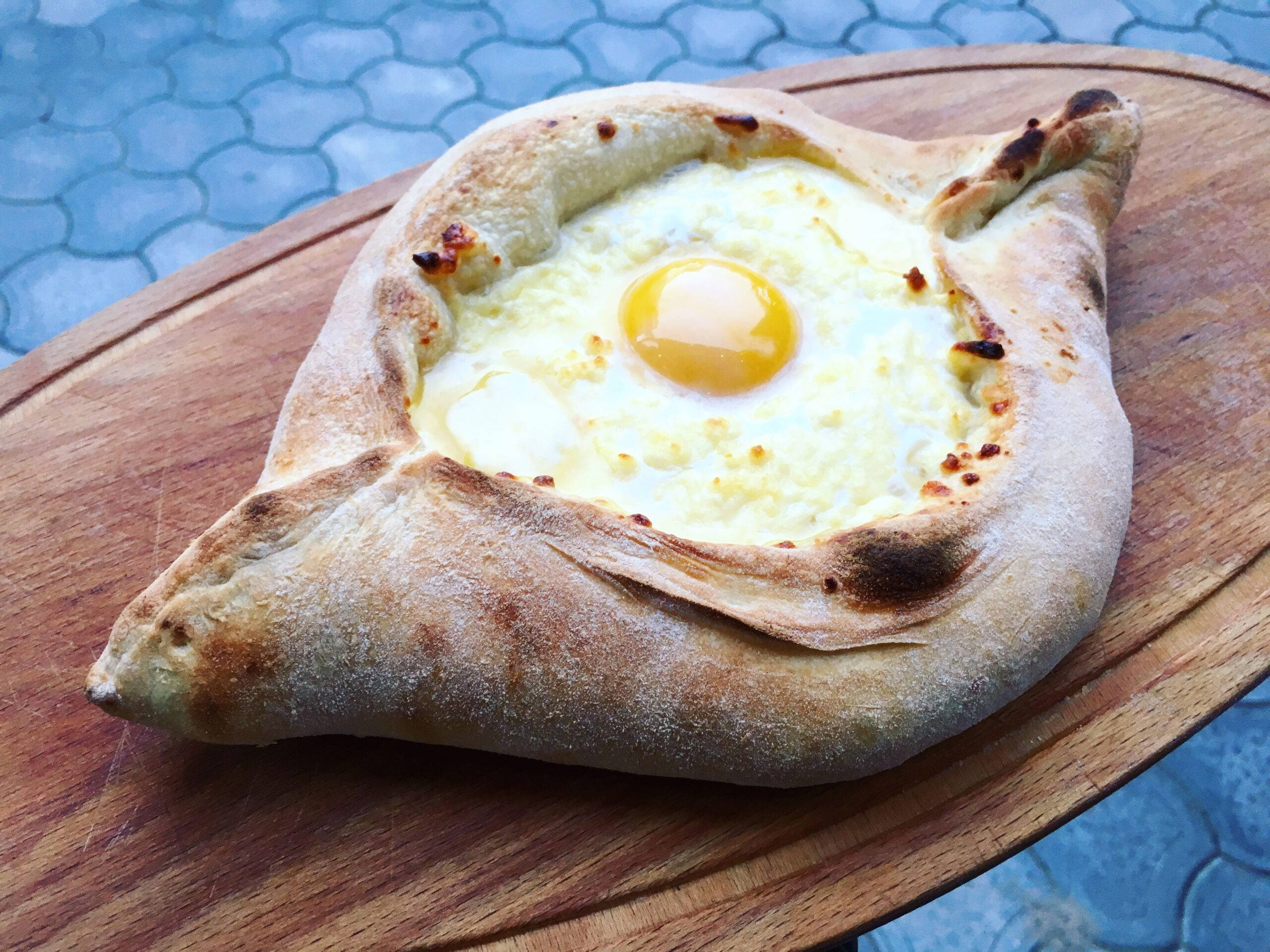 Cheese 桌布 壁紙 — 一個金黃色的哈恰普里（khachapuri）配上半熟蛋黃，放在木板上，背景是藍色磁磚。