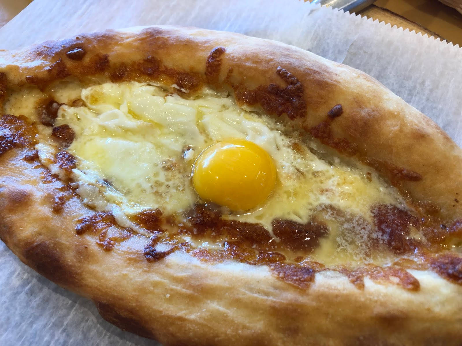 Egg 桌布 壁紙 — 一個金黃色的哈恰普里麵包碗，裡面裝滿了融化的起司和一個完美置中的半熟蛋黃。