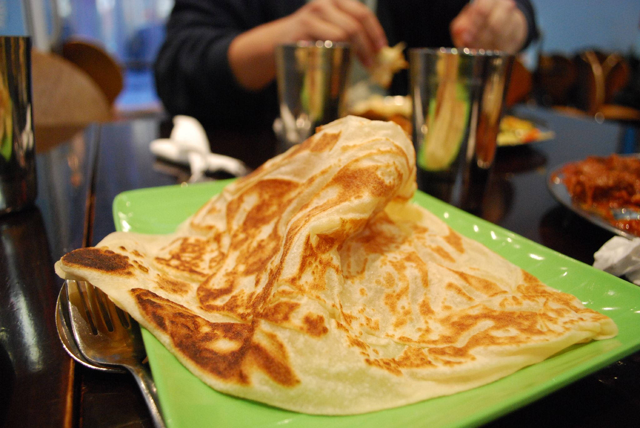 Delicious Food 桌布 壁紙 — 一個金黃色的折疊印度煎餅放在一個亮綠色的盤子上，旁邊有叉子，在餐廳環境中顯得格外誘人。