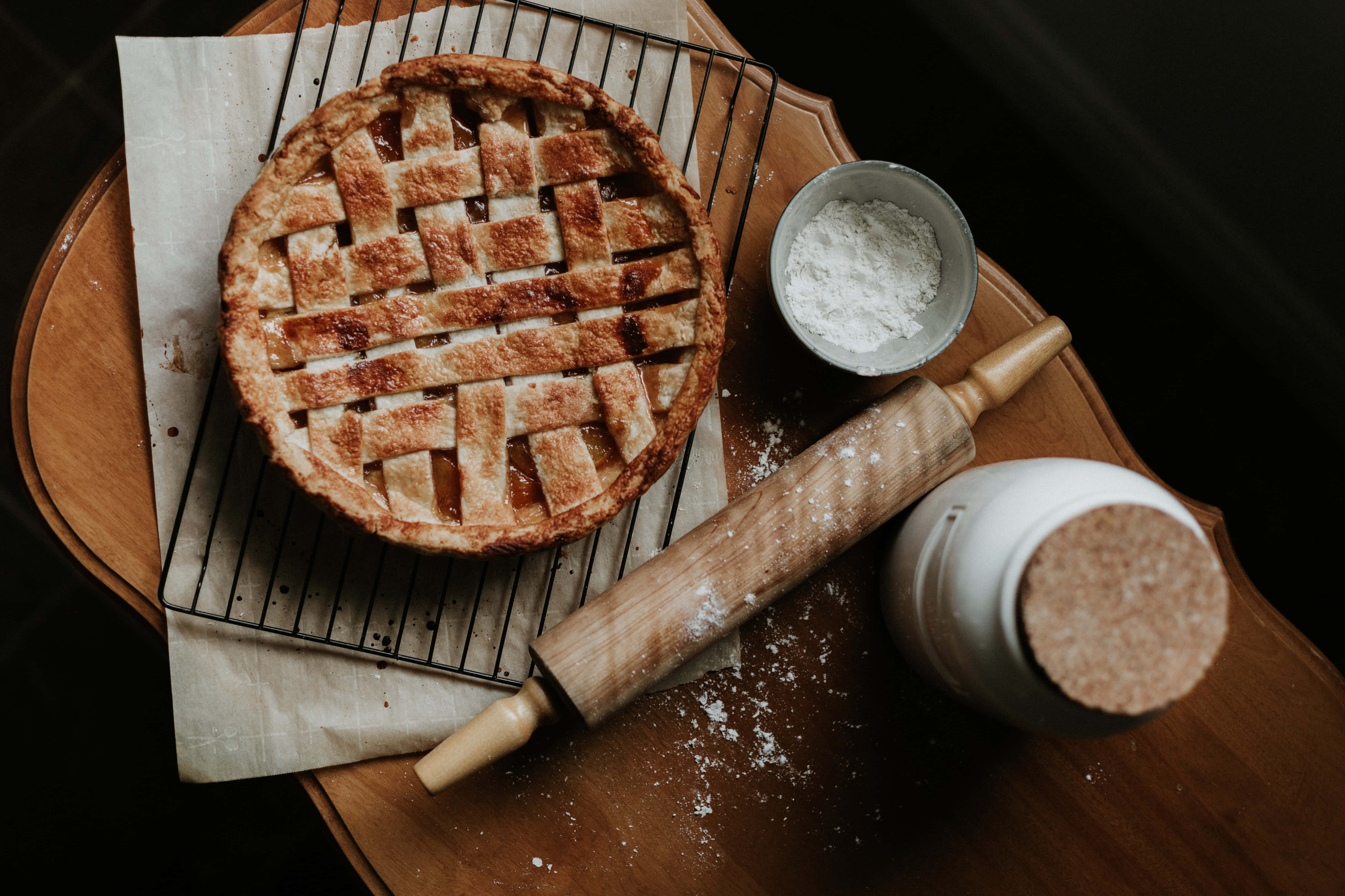 Baking 桌布 壁紙 — 一個金黃色的格子派在金屬架上冷卻，旁邊有擀麵棍和麵粉碗放在木板上。