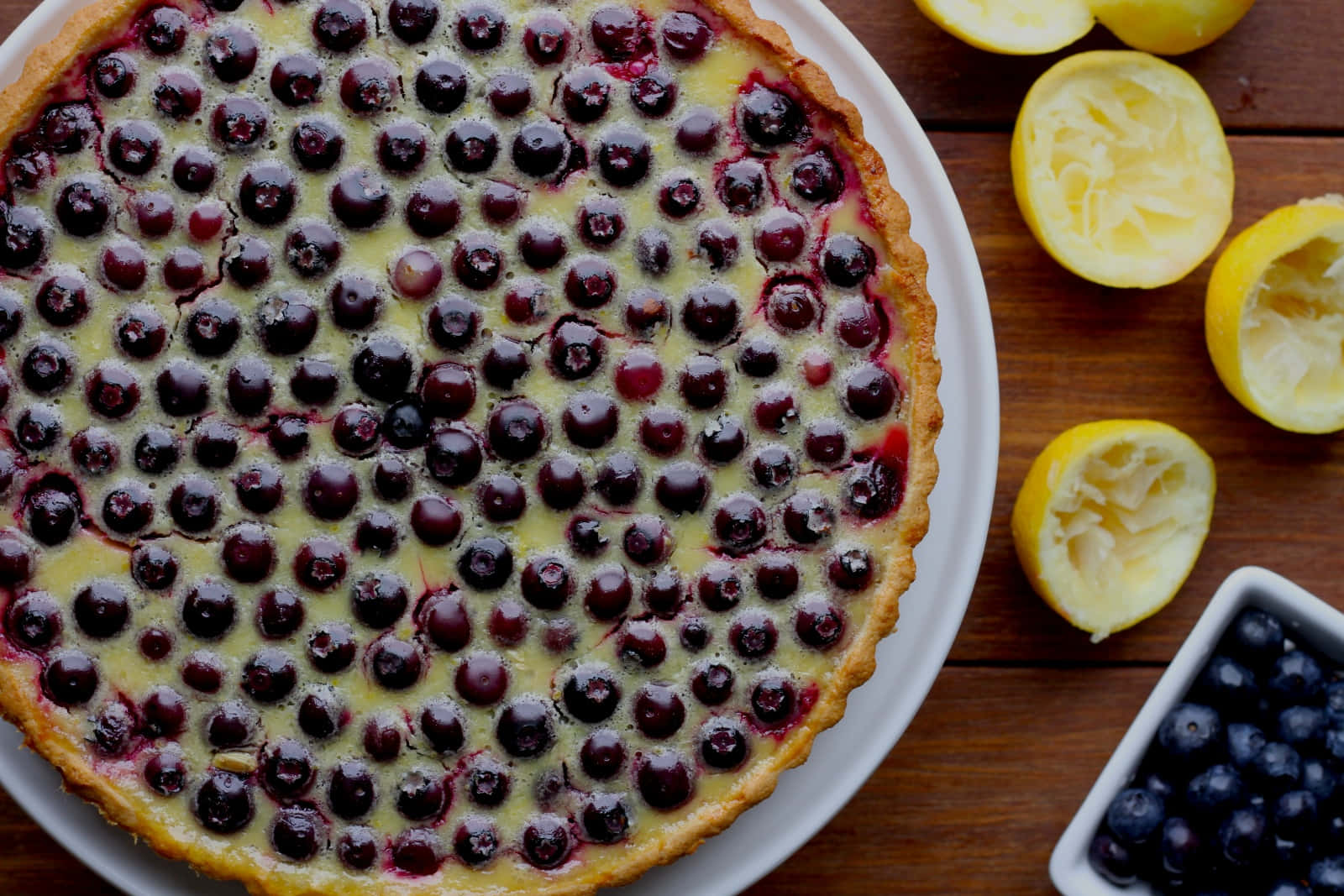 Blueberries Tart 桌布 壁紙 — 一個金黃色的藍莓塔，上面鋪滿新鮮莓果和檸檬半個，放在質樸的木桌上。