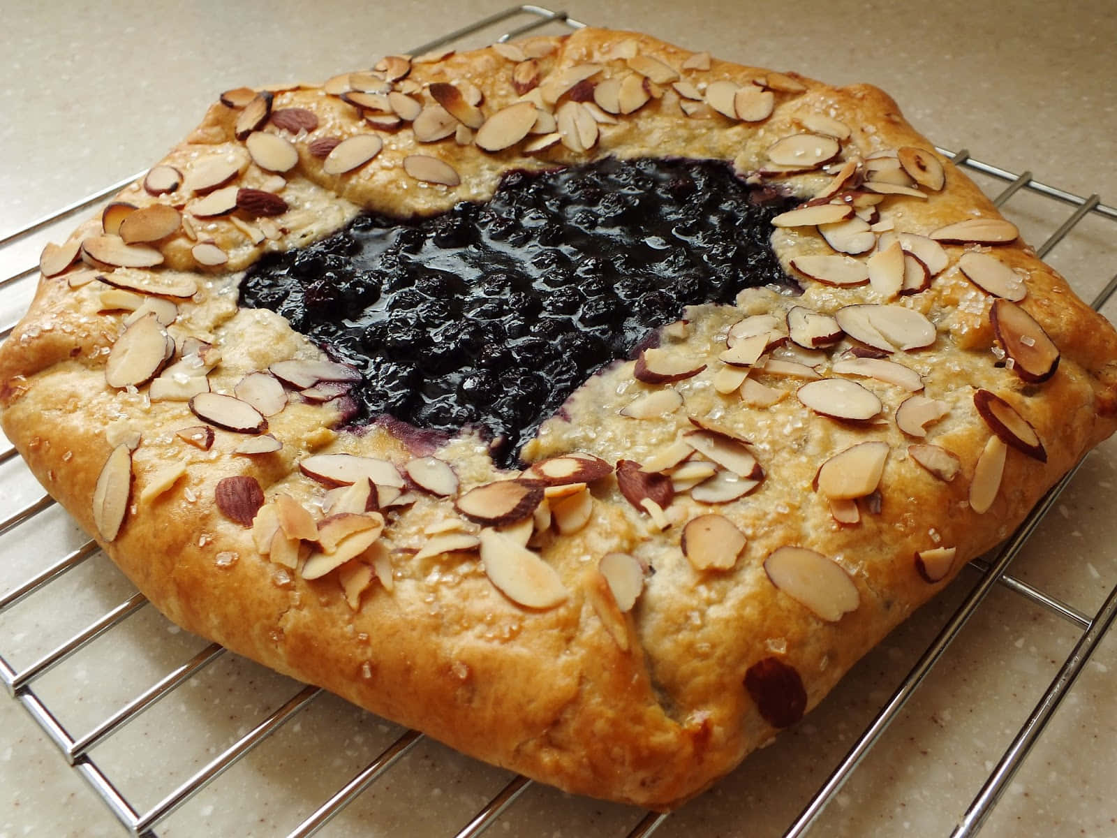 Blueberries Tart 桌布 壁紙 — 一個金黃色的藍莓法式餡餅，上面鋪有杏仁片，正在冷卻架上冷卻。