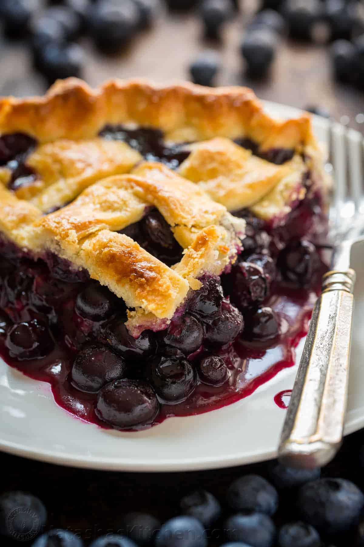 Blueberry Pie 桌布 壁紙 — 一個金黃色的藍莓派，格子狀的派皮上滿是 juicy 的藍莓，放在白色盤子上，特寫鏡頭。