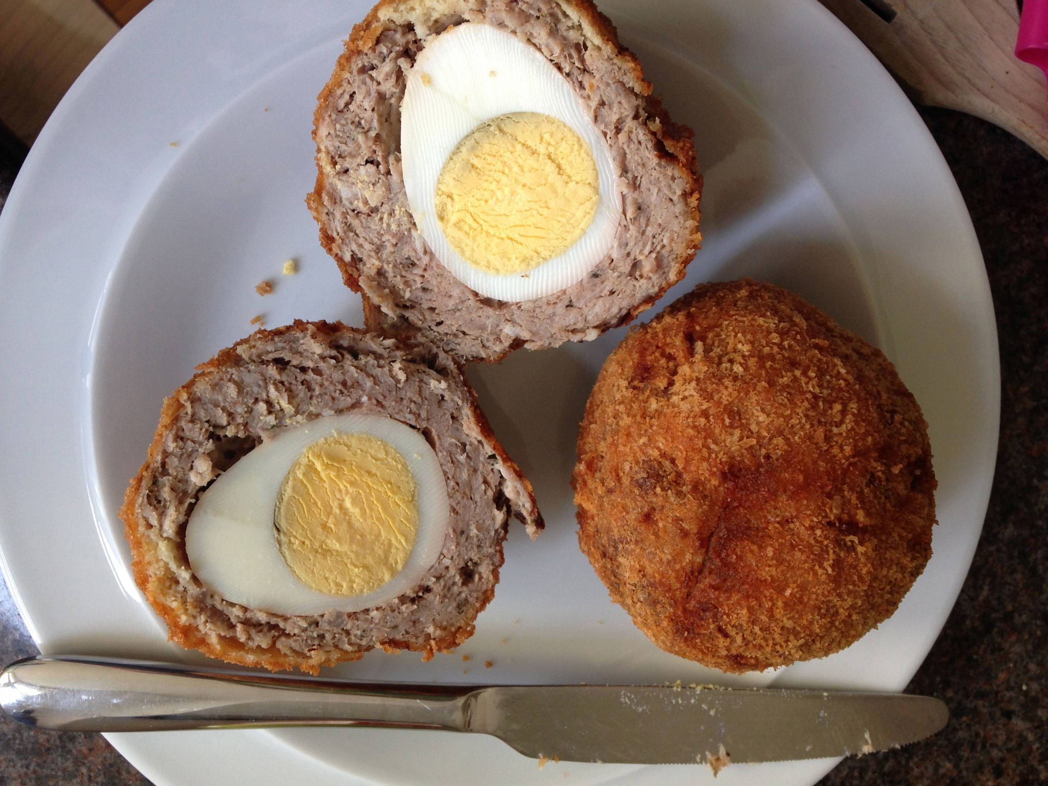Egg 桌布 壁紙 — 一個金黃色的蘇格蘭蛋切成兩半，露出完美煮熟的水煮蛋，包裹在美味的肉餡中，放在白色盤子上。
