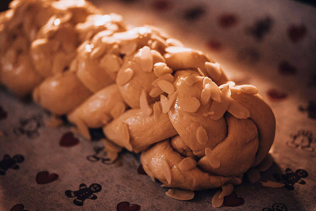 Pretty Christmas 桌布 壁紙 — 一個金黃色的辮子麵包，上面放有切片杏仁，放在圖案布上，在溫暖的燈光下。