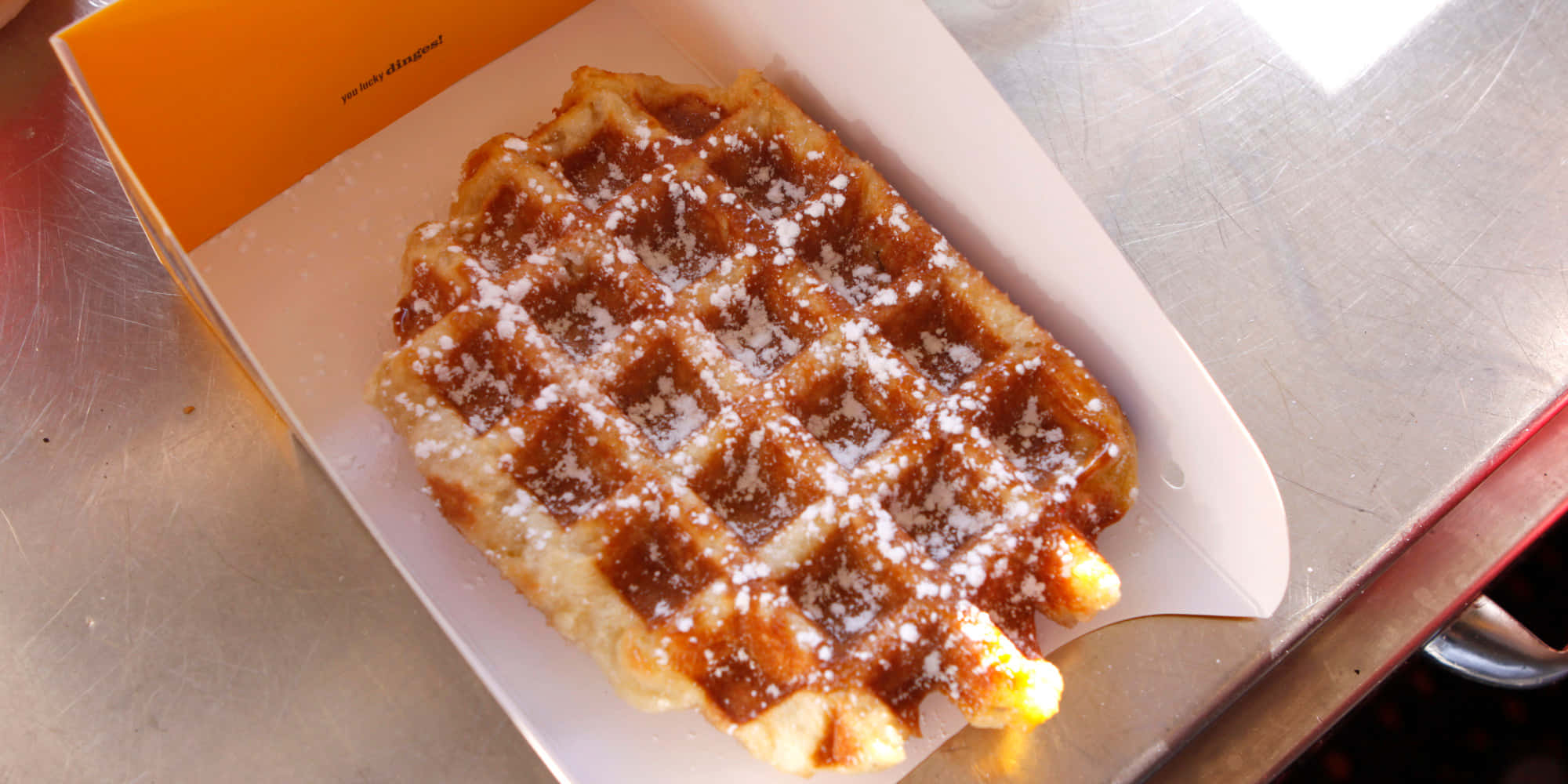 Waffle 桌布 壁紙 — 一個金黃色的鬆餅撒上糖粉，放在不鏽鋼表面的白色紙托盤上。