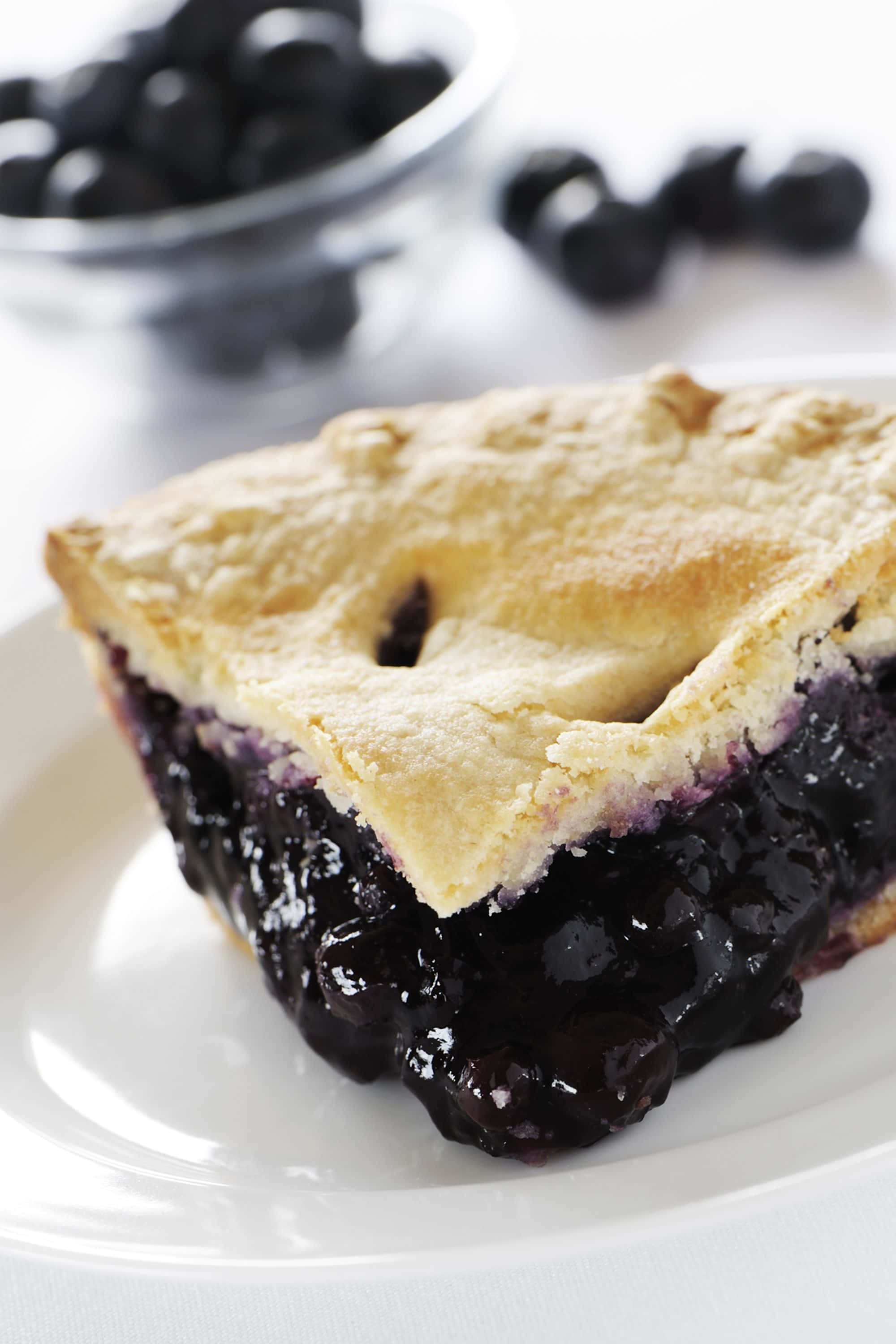 Blueberry Pie 桌布 壁紙 — 一個金黃色藍莓派切件的特寫，帶有豐富的餡料，放在白色盤子上。