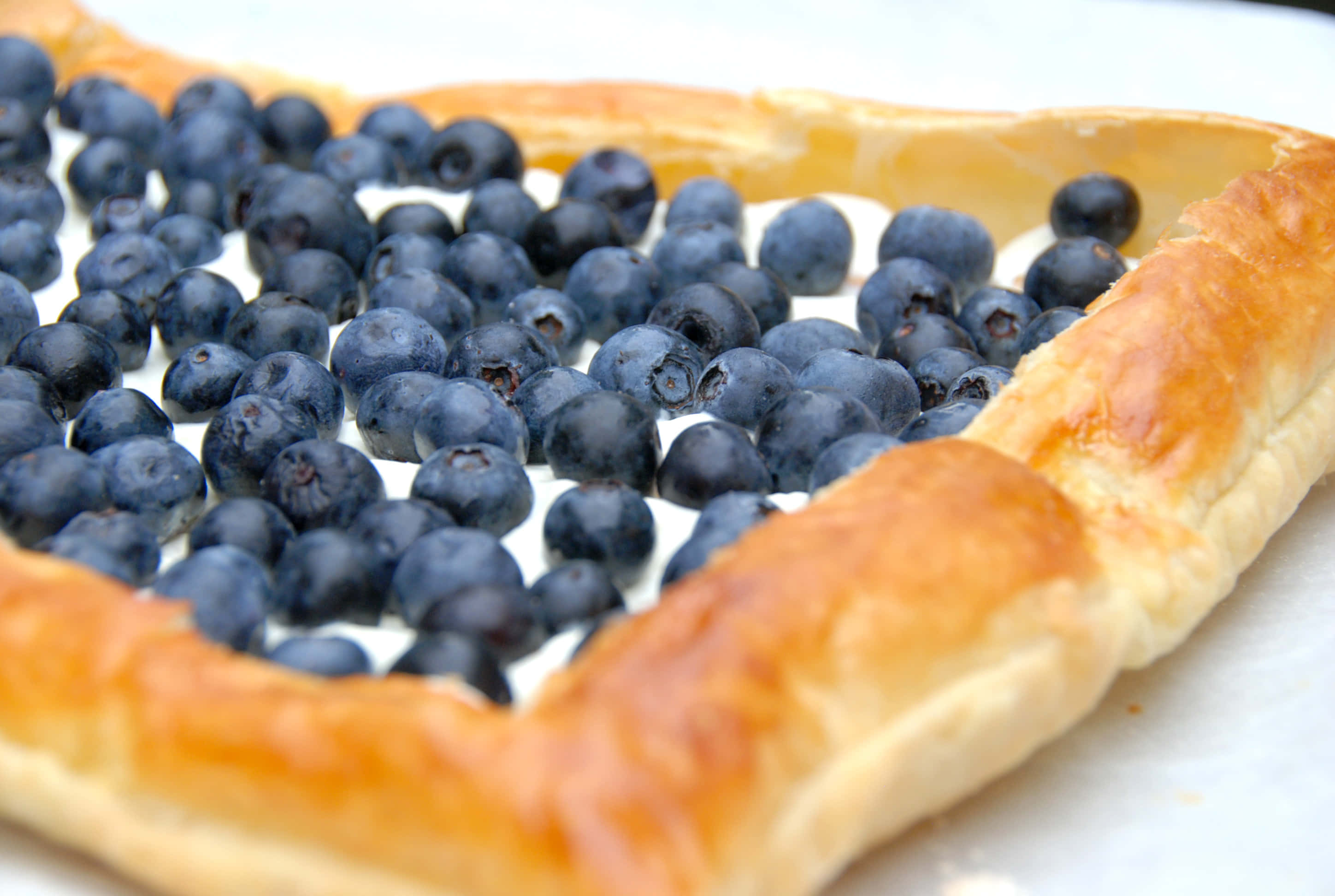 Blueberries Tart 桌布 壁紙 — 一個金黃色酥皮塔的近距離特寫，裡面裝滿了飽滿的藍莓，排列成心形。