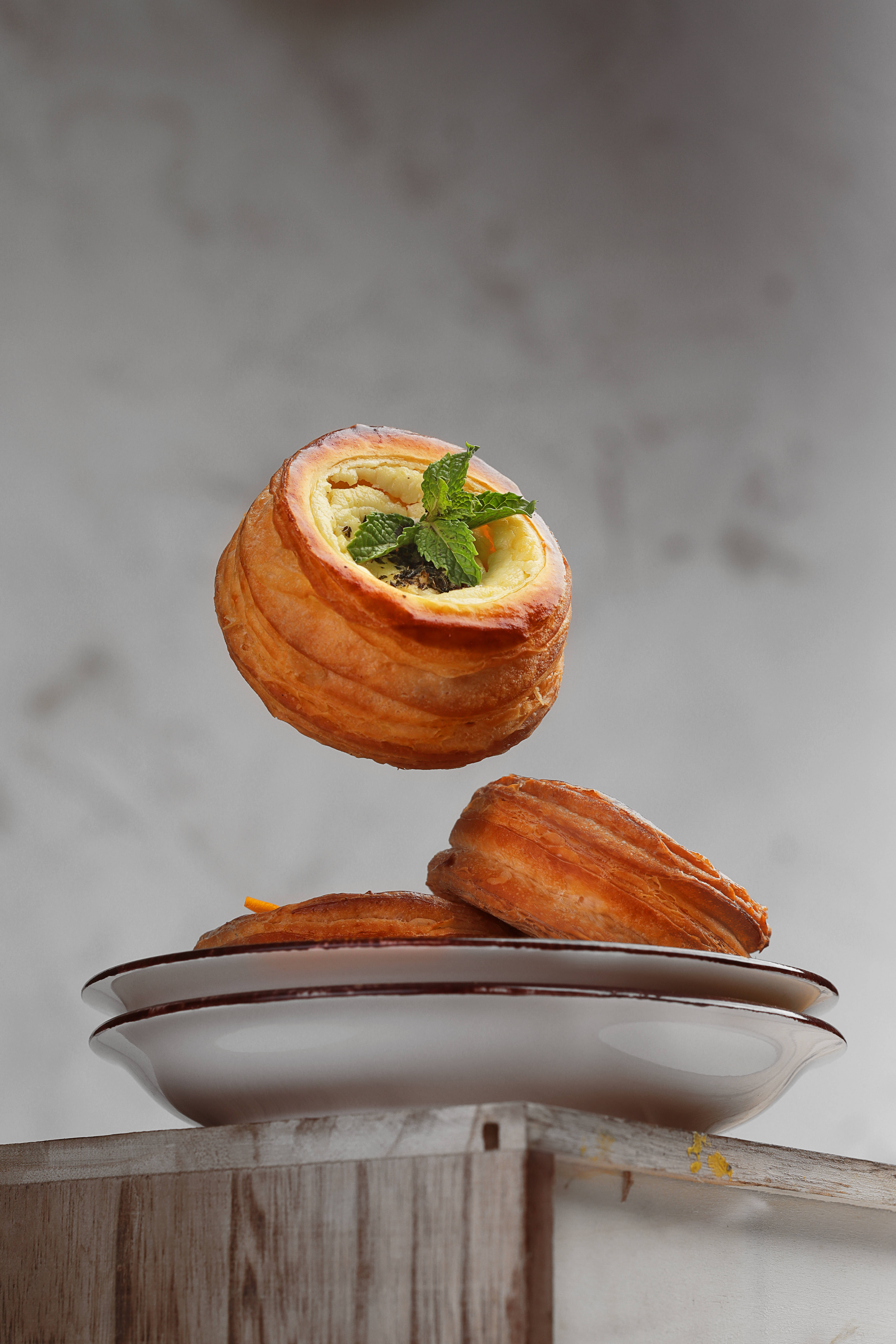 Pastries 桌布 壁紙 — 一個金黃酥脆的糕點，內餡是奶油卡士達和薄荷葉，漂浮在一疊類似糕點之上，放在陶瓷盤上。