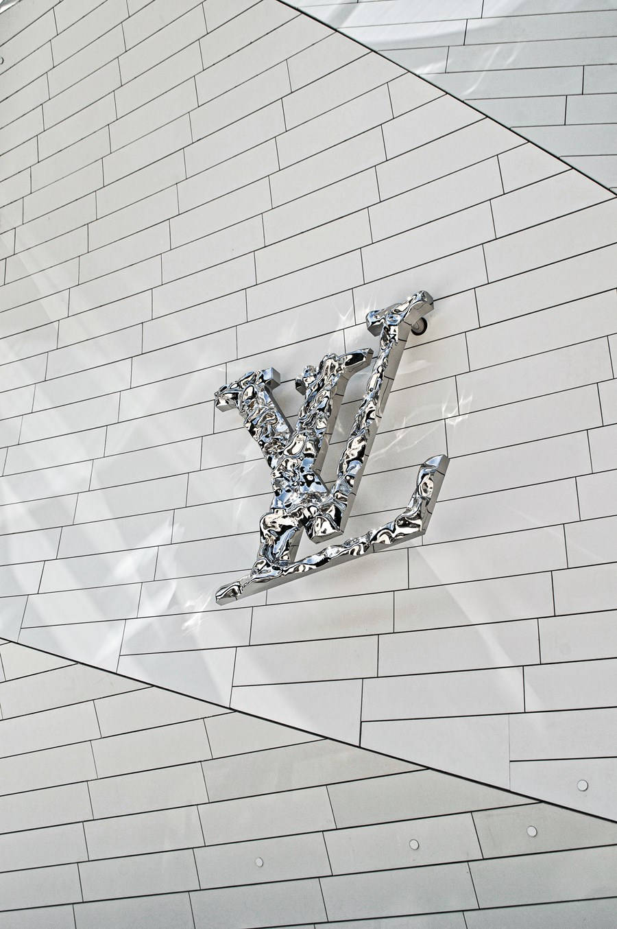 Crystal 桌布 壁紙 — 一個鉻色Louis Vuitton字母組合標誌在帶有幾何陰影的白色瓷磚牆上閃耀。