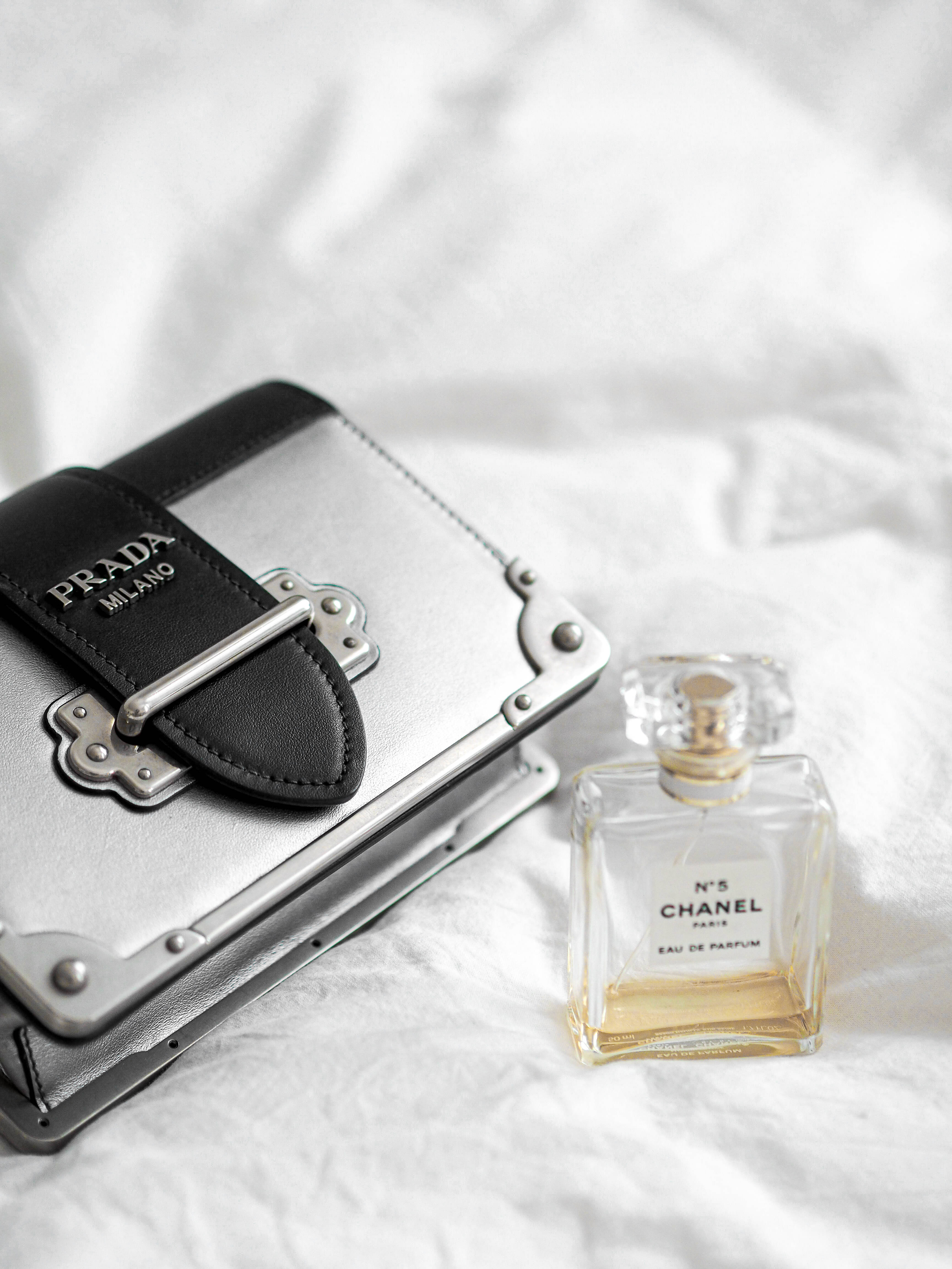 Prada 桌布 壁紙 — 一個銀色Prada錢包和Chanel No 5香水瓶優雅地放在柔軟的白色布料表面上。