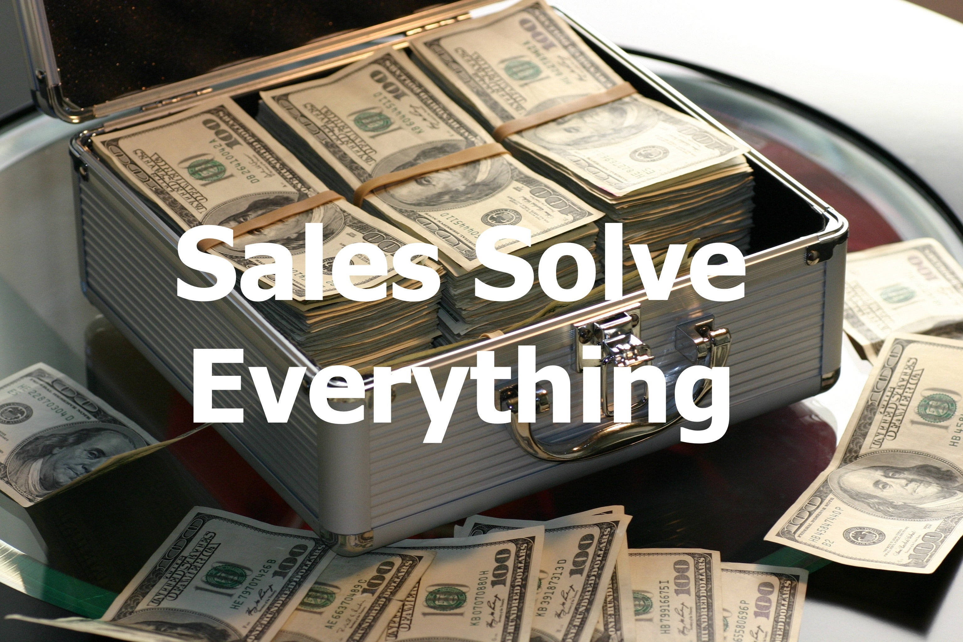 Sales 桌布 壁紙 — 一個銀色公事包裝滿一疊疊100美元鈔票，放在玻璃桌上，周圍散落著現金。
