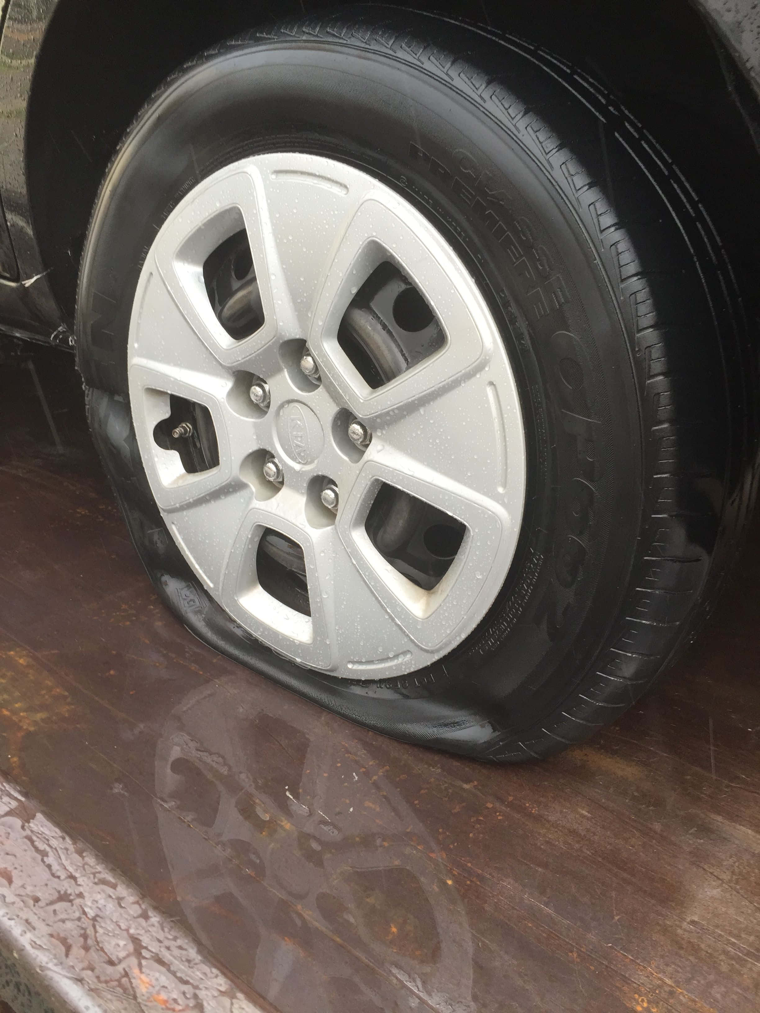 Wheel 桌布 壁紙 — 一個銀色合金輪圈配上扁平輪胎，擱在潮濕木質表面上的特寫。