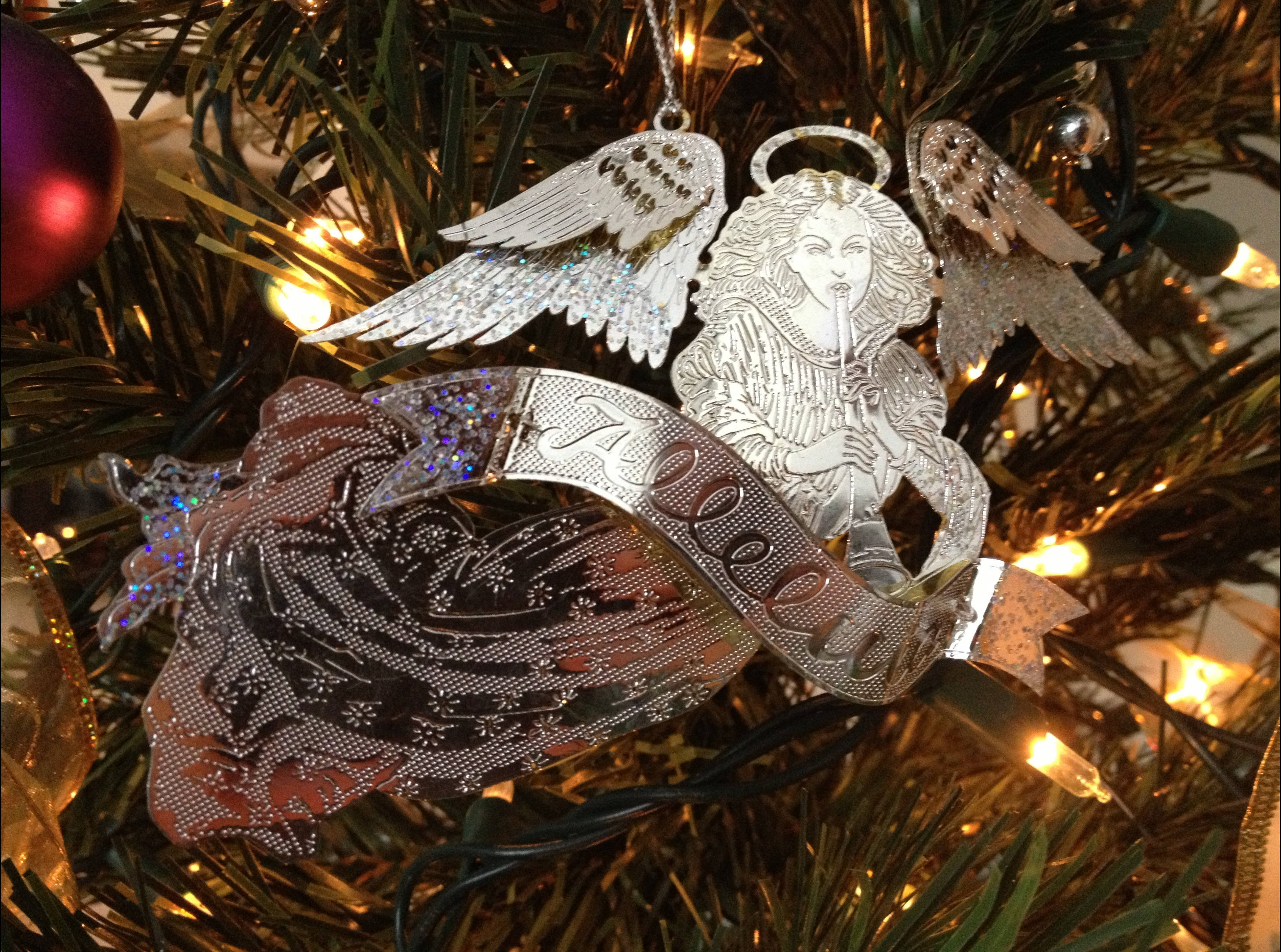 angels 桌布 壁紙 — 一個銀色天使裝飾品，帶有閃閃發光的翅膀和絲帶，掛在點亮的聖誕樹上，樹上有綠色的針葉和溫暖的燈光。
