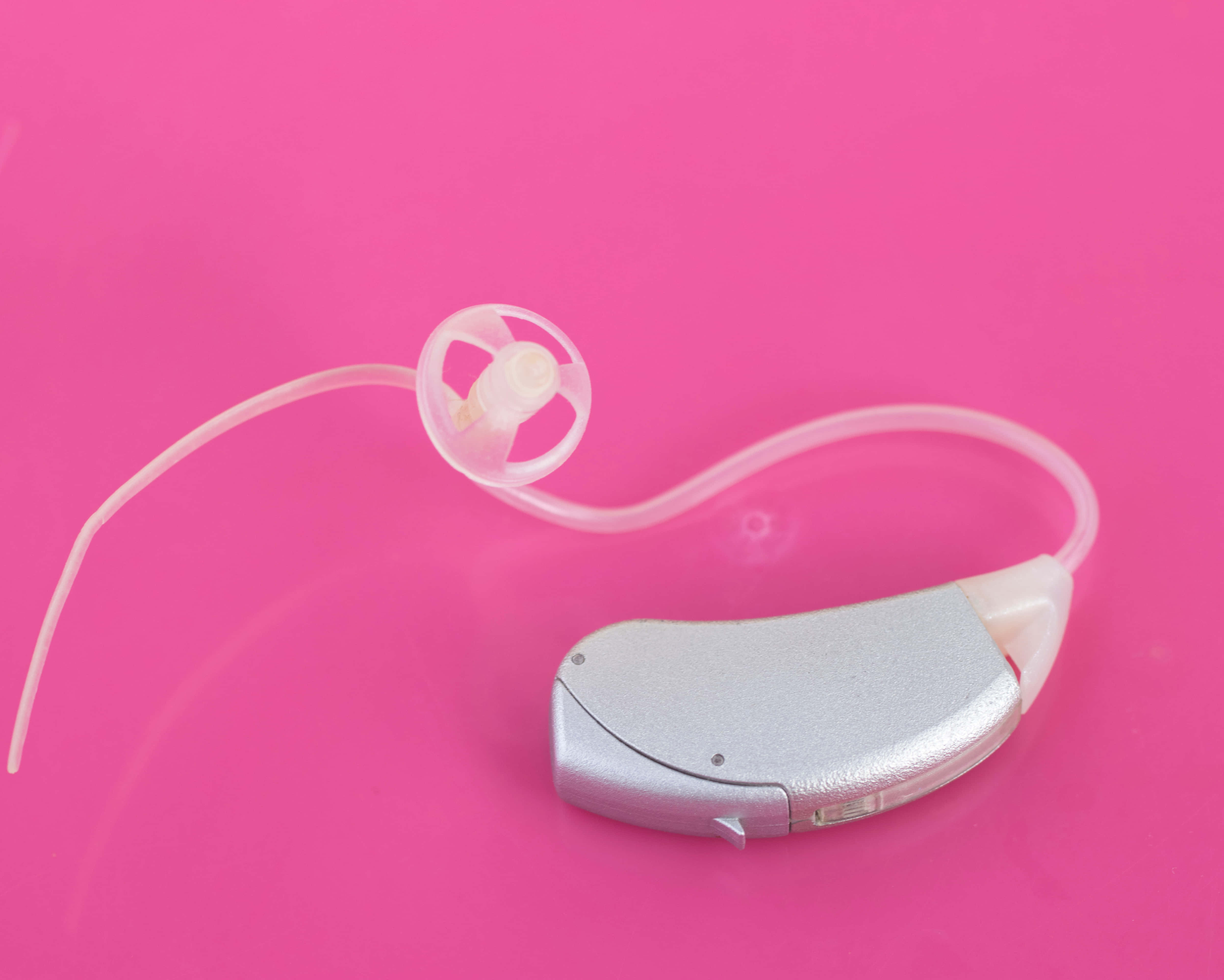 Hearing Aid 桌布 壁紙 — 一個銀色耳背式助聽器連透明導管放在鮮粉紅色背景上。