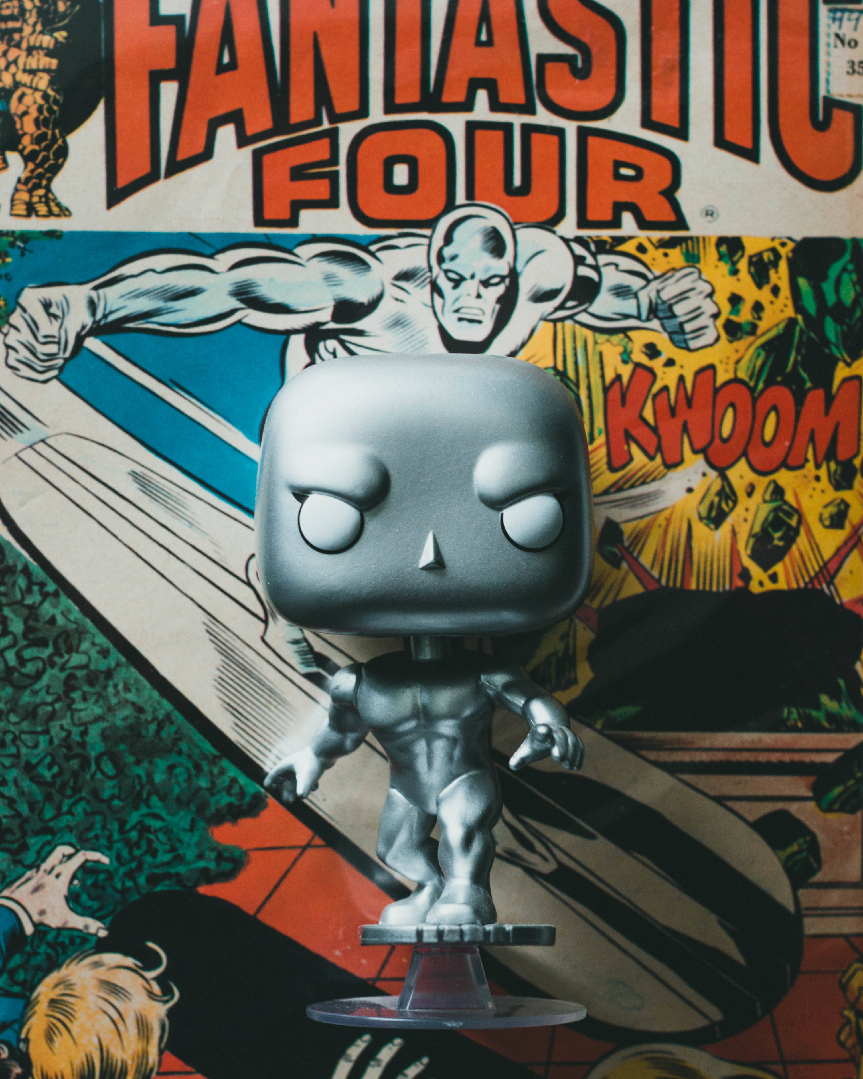 pop 桌布 壁紙 — 一個銀色金屬質感的Funko Pop！驚奇四超人銀色衝浪手人偶，站在透明底座上，背景是復古漫畫封面。
