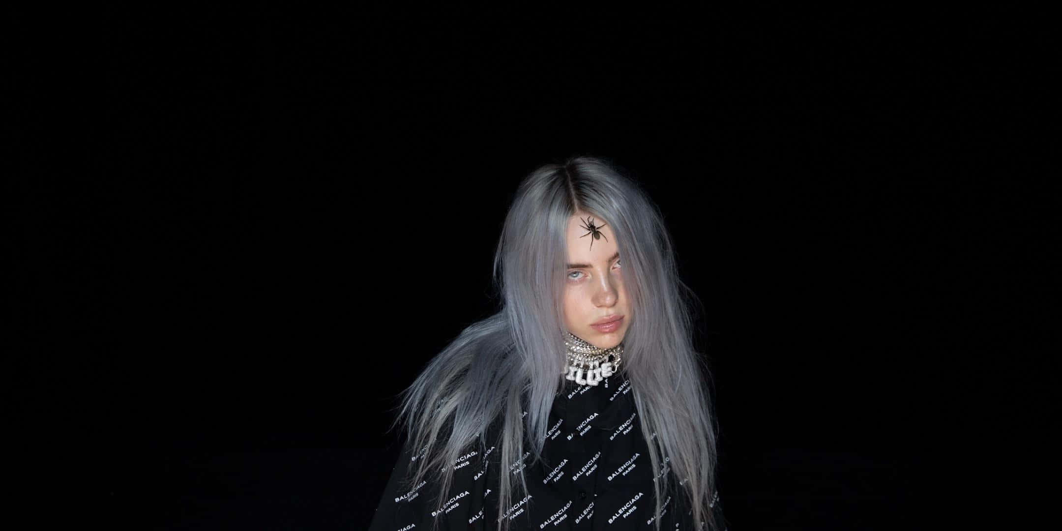 Billie Eilish Laptop 桌布 壁紙 — 一個銀色頭髮、額頭上有蜘蛛刺青的人，在黑色背景下強烈地凝視。