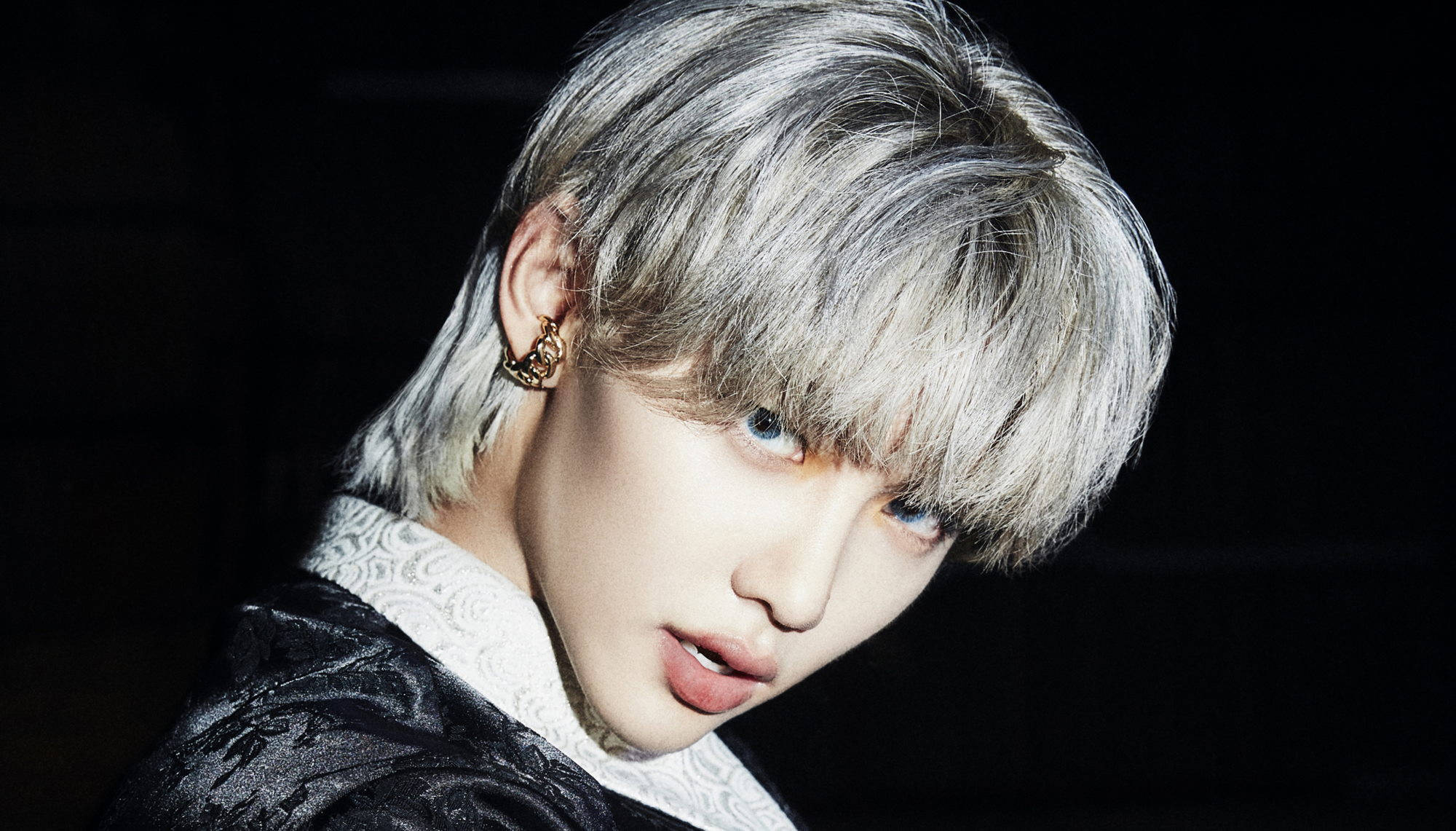 Stray Kids 桌布 壁紙 — 一個銀色頭髮和藍色眼睛的人，在深色背景下穿著黑色紋理外套，內搭白色蕾絲領，凝視著。