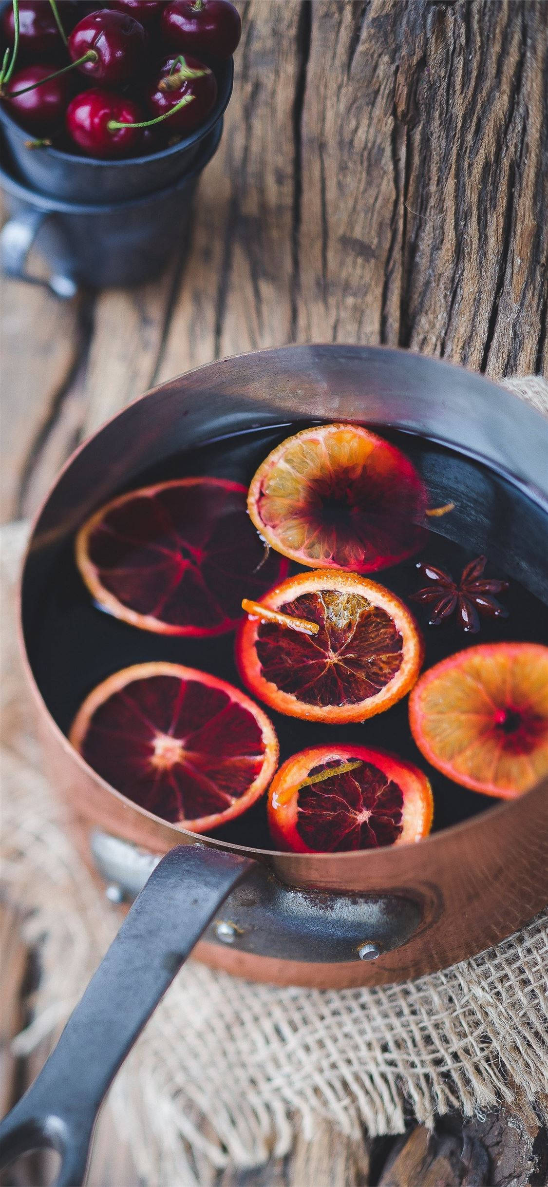 Fruit 桌布 壁紙 — 一個銅鍋裝滿深色熱紅酒和橙片，放在一個鄉村風格的木桌上，旁邊有一碗櫻桃。