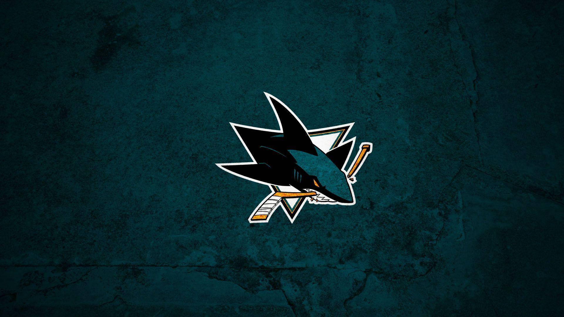 sharks 桌布 壁紙 — 一個鋒利的鯊魚標誌，帶有交叉的曲棍球棒，居中在帶有紋理的深青色背景上。