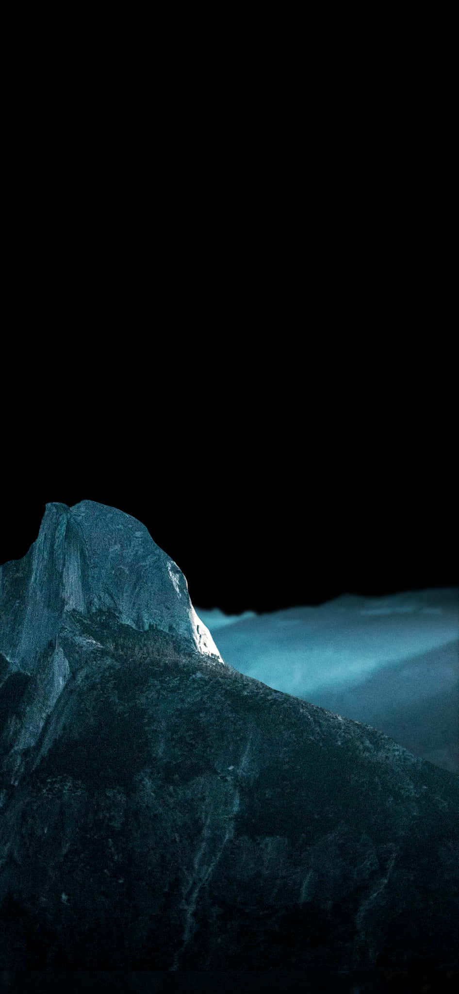 iPhone X Oled 桌布 壁紙 — 一個鋸齒狀的山峰在漆黑的天空和霧氣瀰漫的山谷上方散發出冷藍色的光芒。