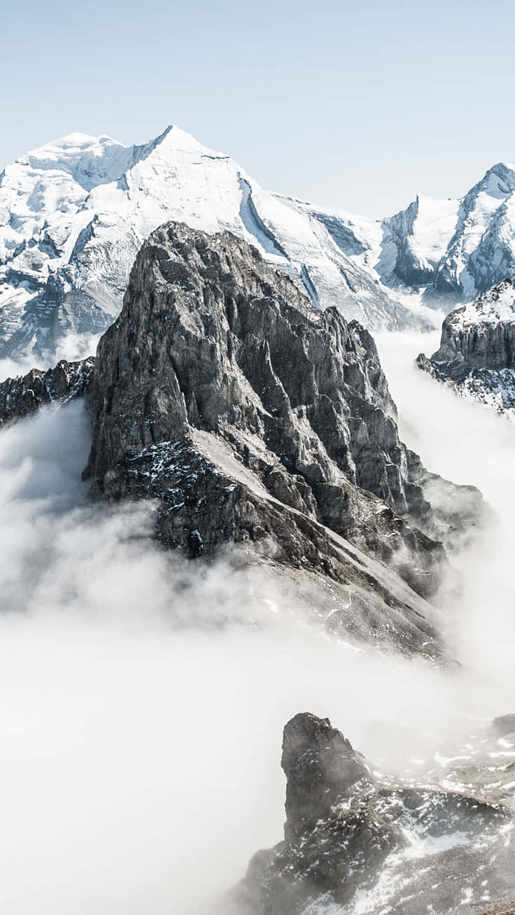 桌布 壁紙 — 一個鋸齒狀的積雪山峰在旋轉的雲層上方升起，頭頂是清澈的藍天。