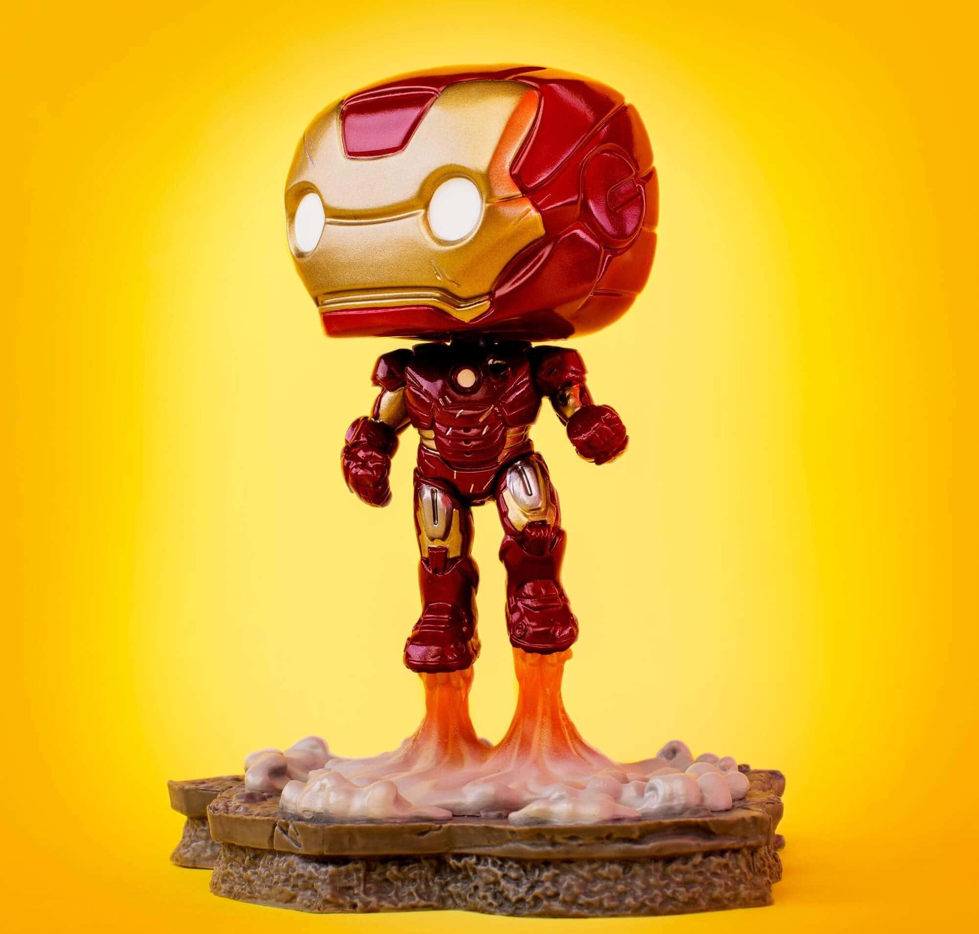 Iron Man Pop Figures 桌布 壁紙 — 一個鋼鐵人的Funko Pop!人偶站在岩石底座上，雙腳發光，背景是鮮豔的黃色漸層。
