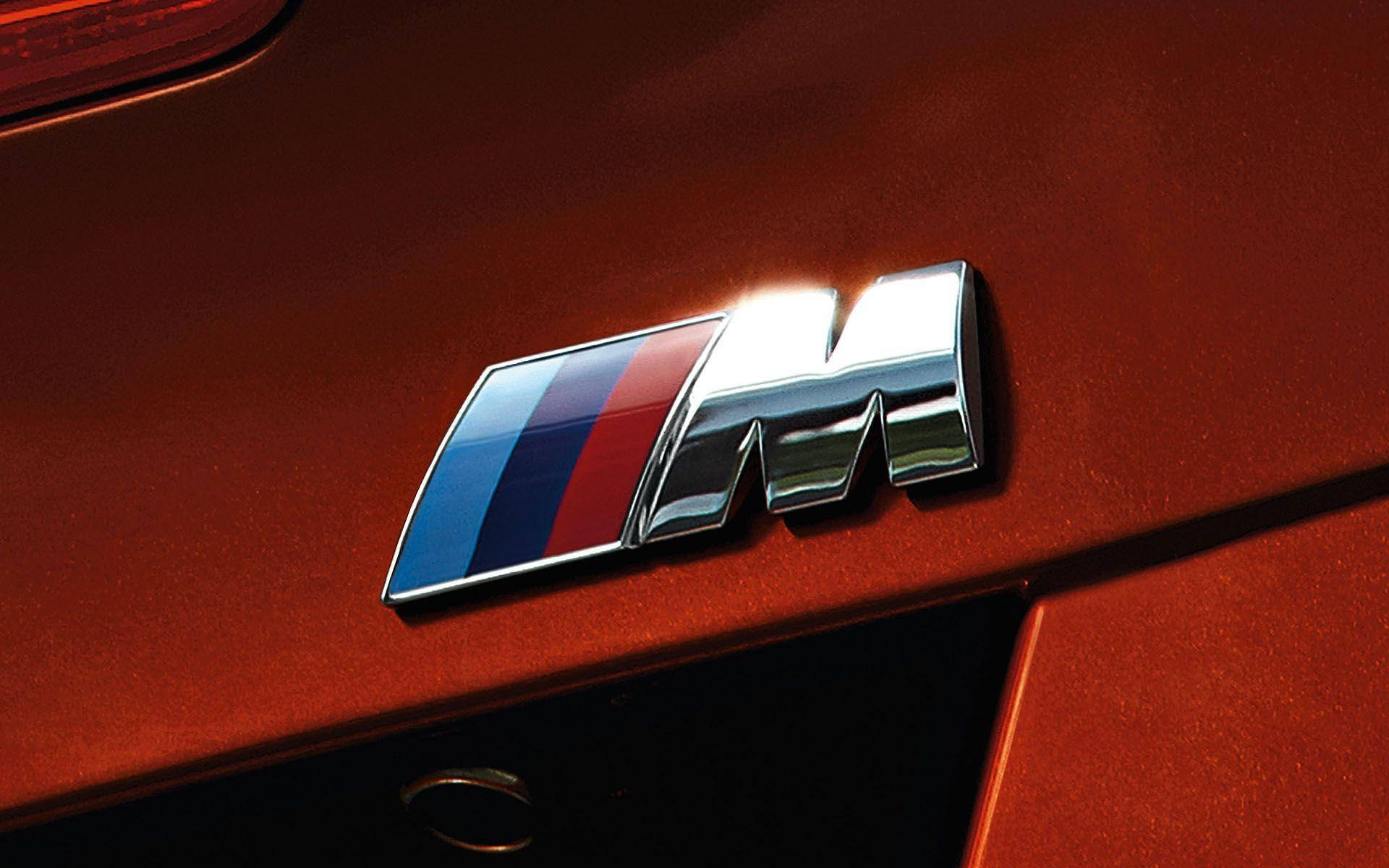 Logo 桌布 壁紙 — 一個鍍鉻BMW M徽章的近距離特寫，帶有藍色和紅色條紋，在光亮的紅色引擎蓋上閃閃發光。