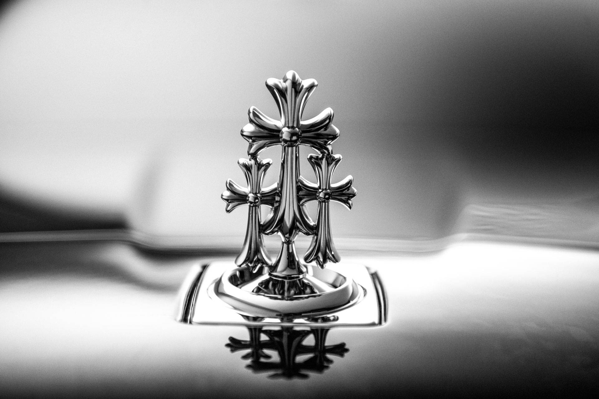 Chrome Hearts 桌布 壁紙 — 一個鍍鉻勞斯萊斯格柵飾件的單色特寫，上面有三個華麗的十字架，反射在拋光表面上。