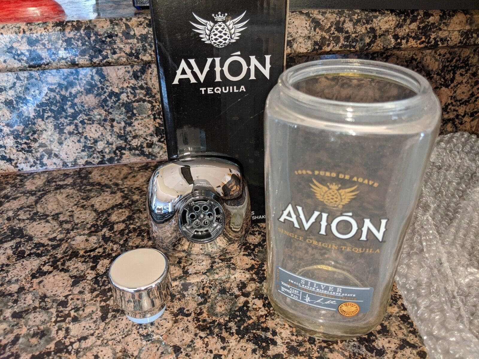 bottle 桌布 壁紙 — 一個鍍鉻雞尾酒調酒器和一個空的Avion龍舌蘭酒瓶放在斑點花崗岩檯面上，旁邊是它的黑色盒子。
