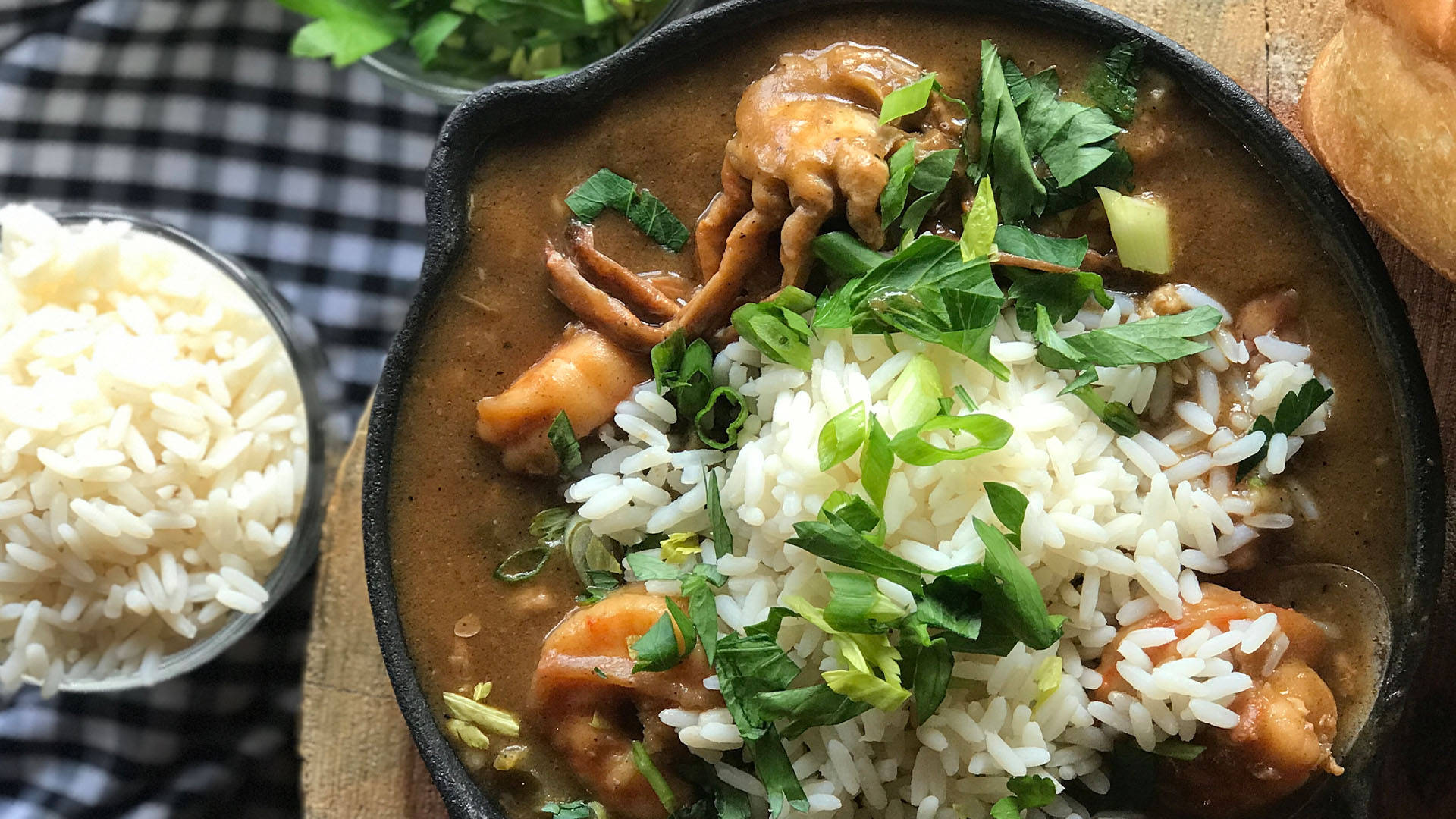 Rice 桌布 壁紙 — 一個鑄鐵煎鍋，盛滿濃郁的棕色海鮮秋葵湯，上面放著白米和新鮮的綠色香草。