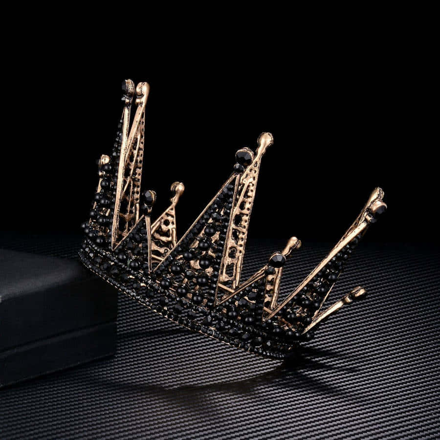 Crown 桌布 壁紙 — 一個鑲有寶石、帶有骷髏圖案的金黑相間皇冠，優雅地放置在深色背景下的紋理黑色表面上。