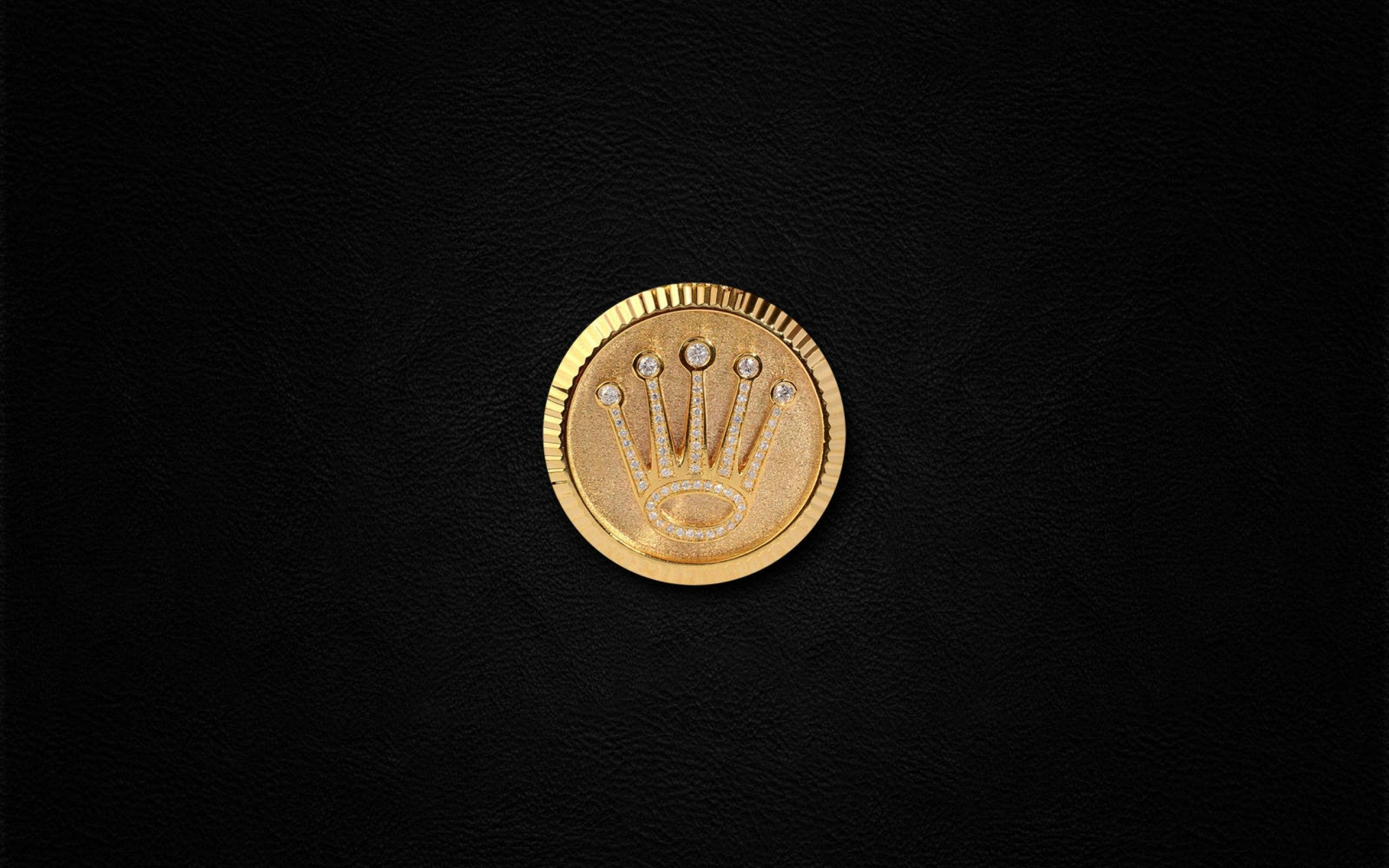 Rolex 桌布 壁紙 — 一個鑲有鑽石的金色勞力士皇冠標誌，居中放置在帶有紋理的黑色皮革表面上。