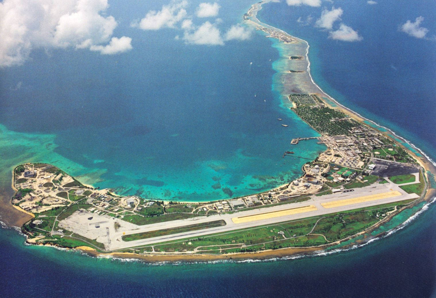 島嶼 桌布 壁紙 — 一個長形熱帶島嶼的鳥瞰圖，島上有一個跑道機場，周圍環繞著碧綠色的潟湖和深藍色的海洋。